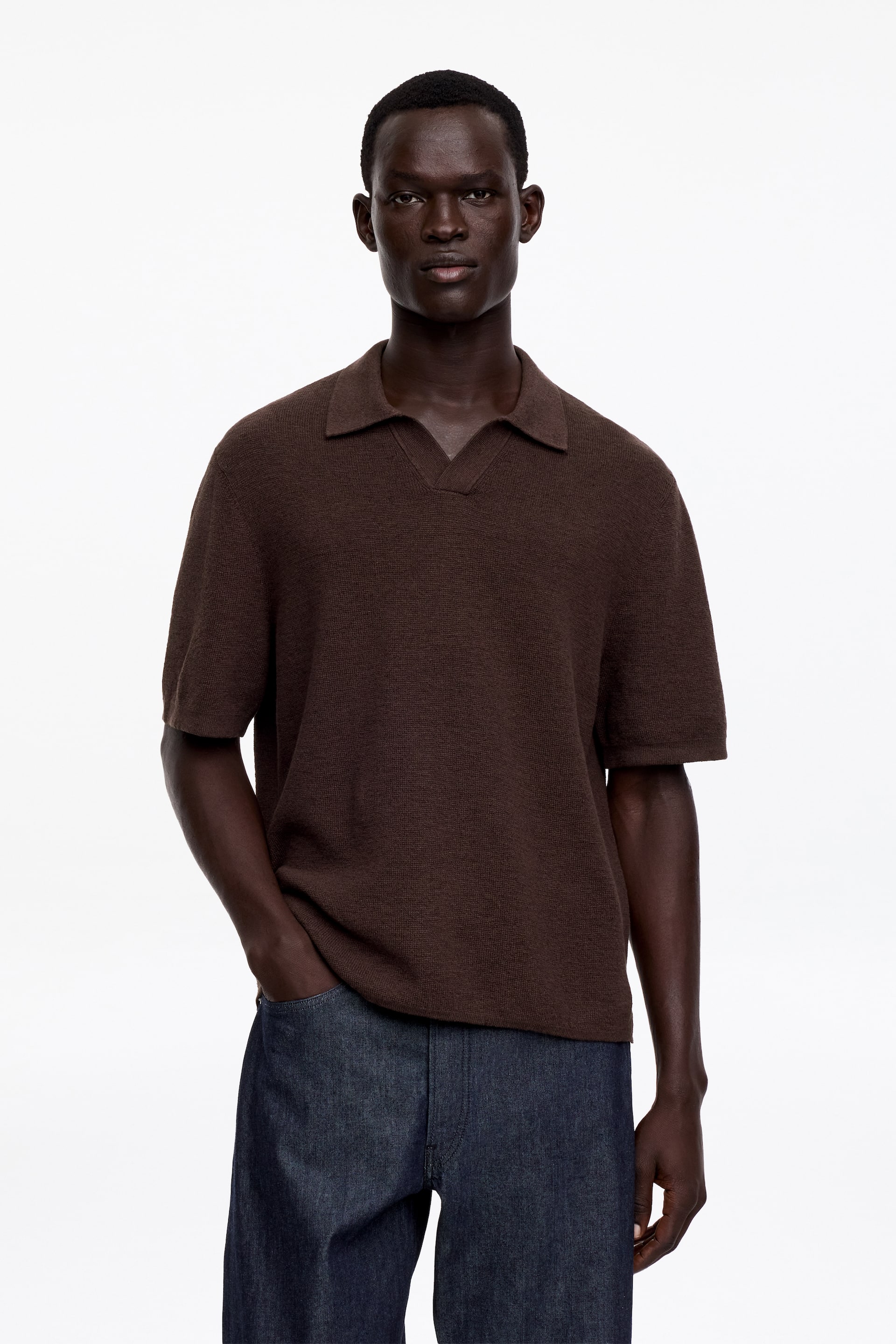 View larger image: A brown short-sleeve polo shirt, featuring a subtle mélange effect and knitted in a half Milano stitch, is being worn by the model. It has an open polo collar with a V-neck, and is finished with clean tubular cuffs and bottom hem.