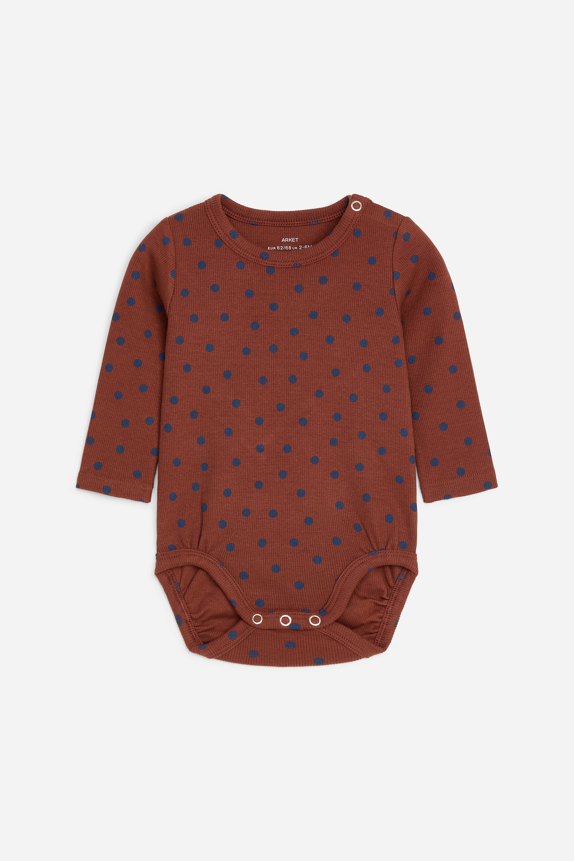 Visa större bild: En brun babybody med blå prickar ligger platt med framsidan uppåt, och har en rund halsringning och långa ärmar. Den visar en subtil ribbad struktur, med en vit tryckknappsstängning på vänster axel och tre vita tryckknappar i grenen.