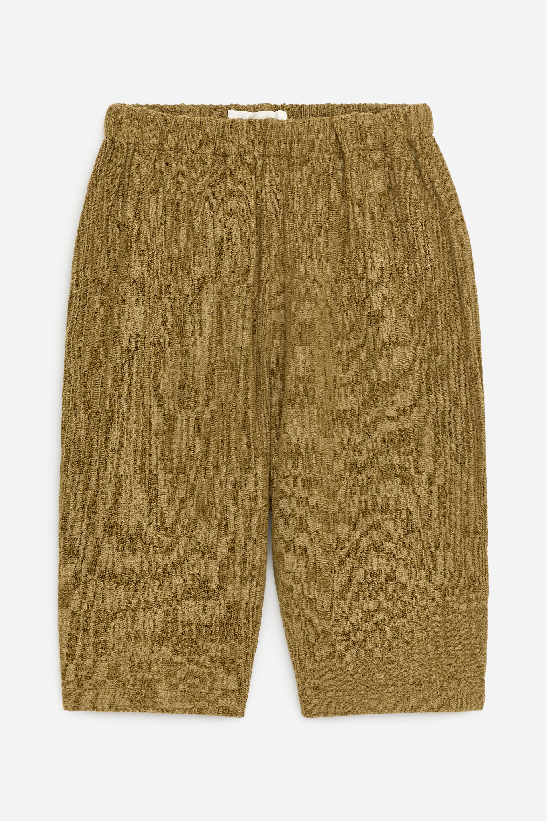 Zobacz większy obraz: Para oliwkowozielonych, luźno dopasowanych spodni prezentowana jest od przodu. Wykonane są z miękkiej, teksturowanej tkaniny muślinowej i posiadają elastyczny, regulowany pas.