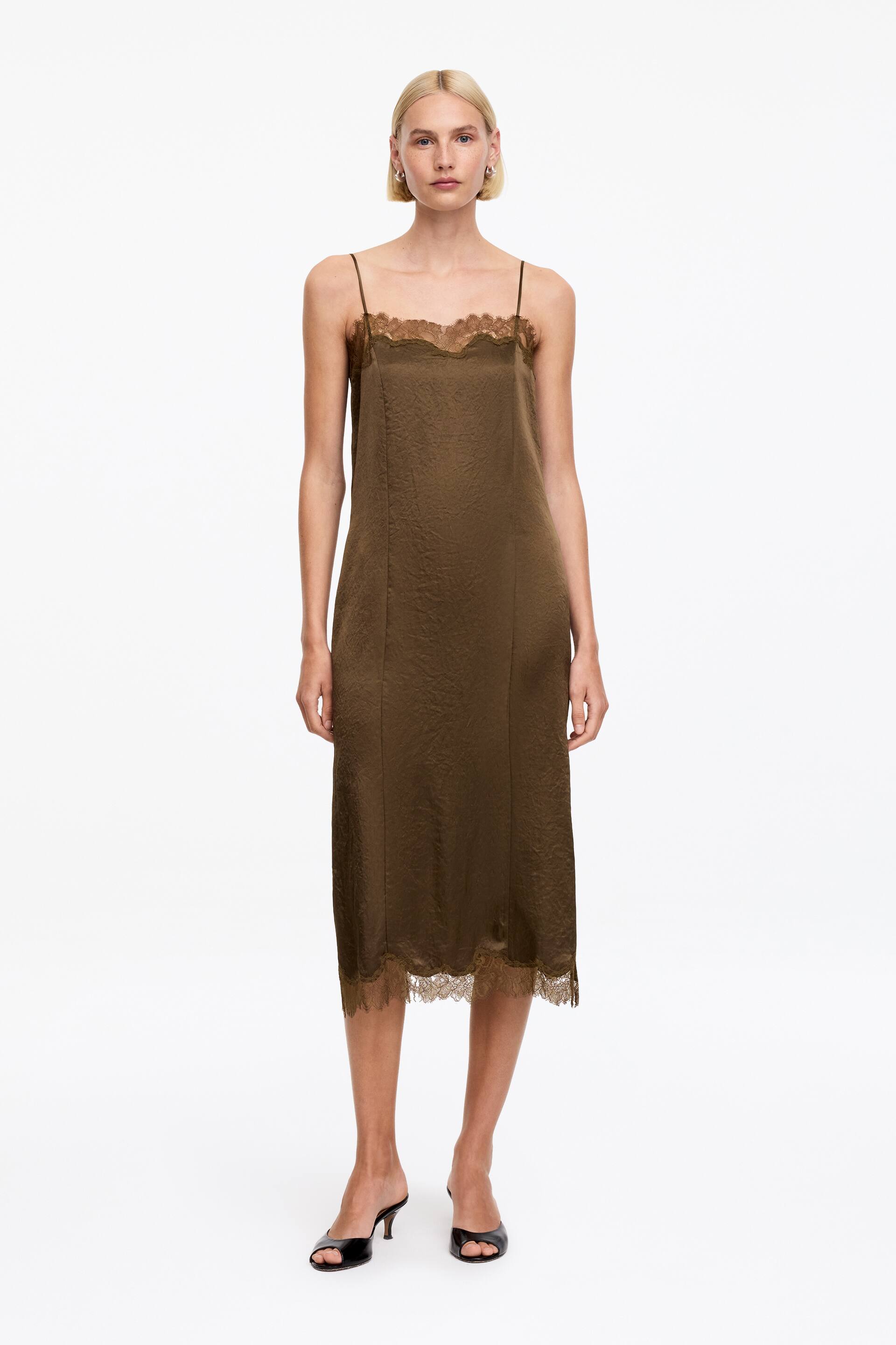 Ver imagen más grande: Un vestido lencero verde caqui está de frente, mostrando un tejido con acabado satinado texturizado. Está diseñado con delicados tirantes finos, un escote redondeado y un ribete de encaje que adorna tanto el escote como el dobladillo de largo midi.