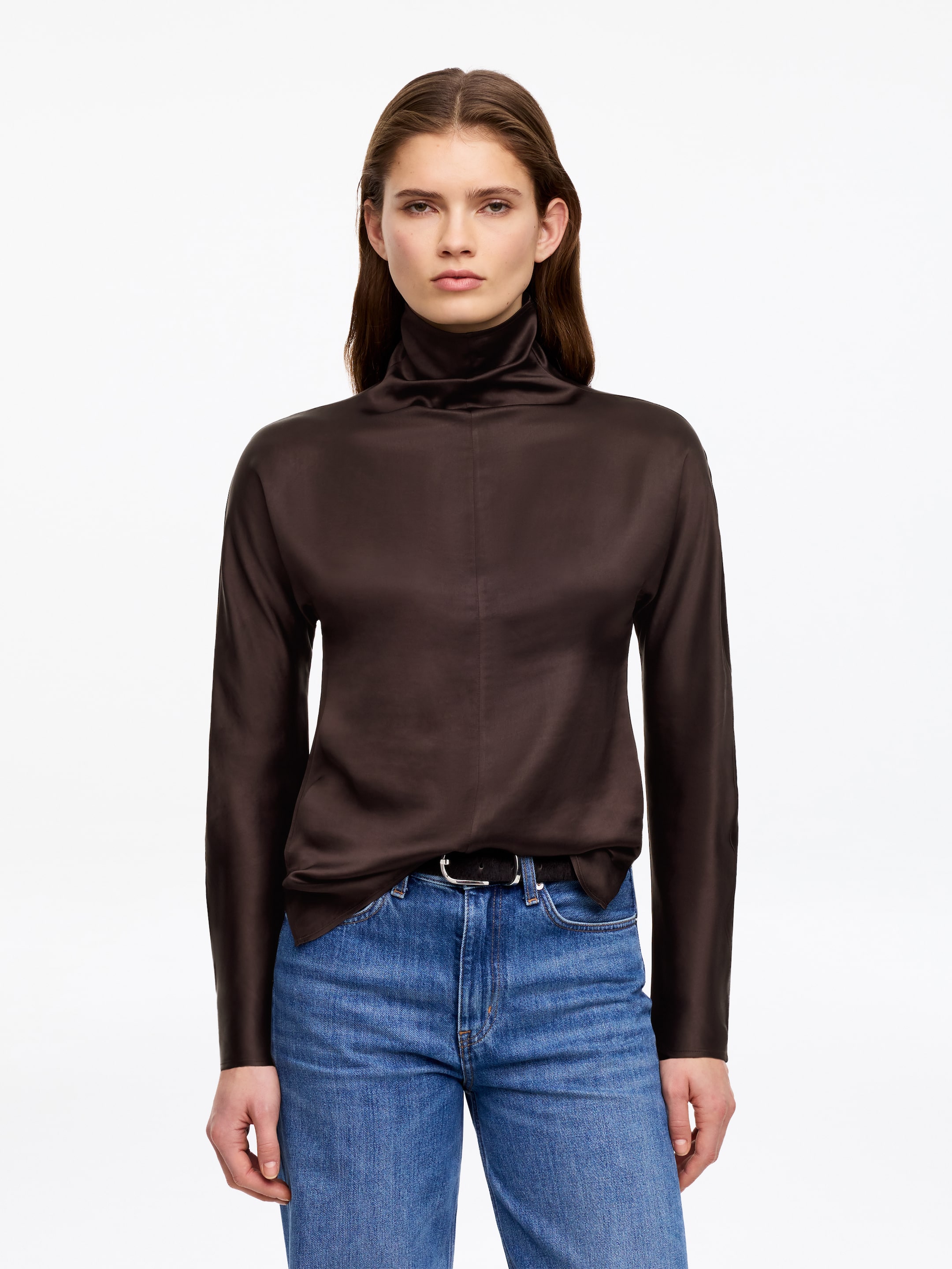 Προβολή μεγαλύτερης εικόνας: Ένα σκούρο καφέ ζιβάγκο τοπ παρουσιάζει ένα λείο ύφασμα με σατινέ φινίρισμα και μακριά μανίκια. Φοριέται μέσα από μπλε τζιν, με μια μαύρη ζώνη να φαίνεται στη μέση.
