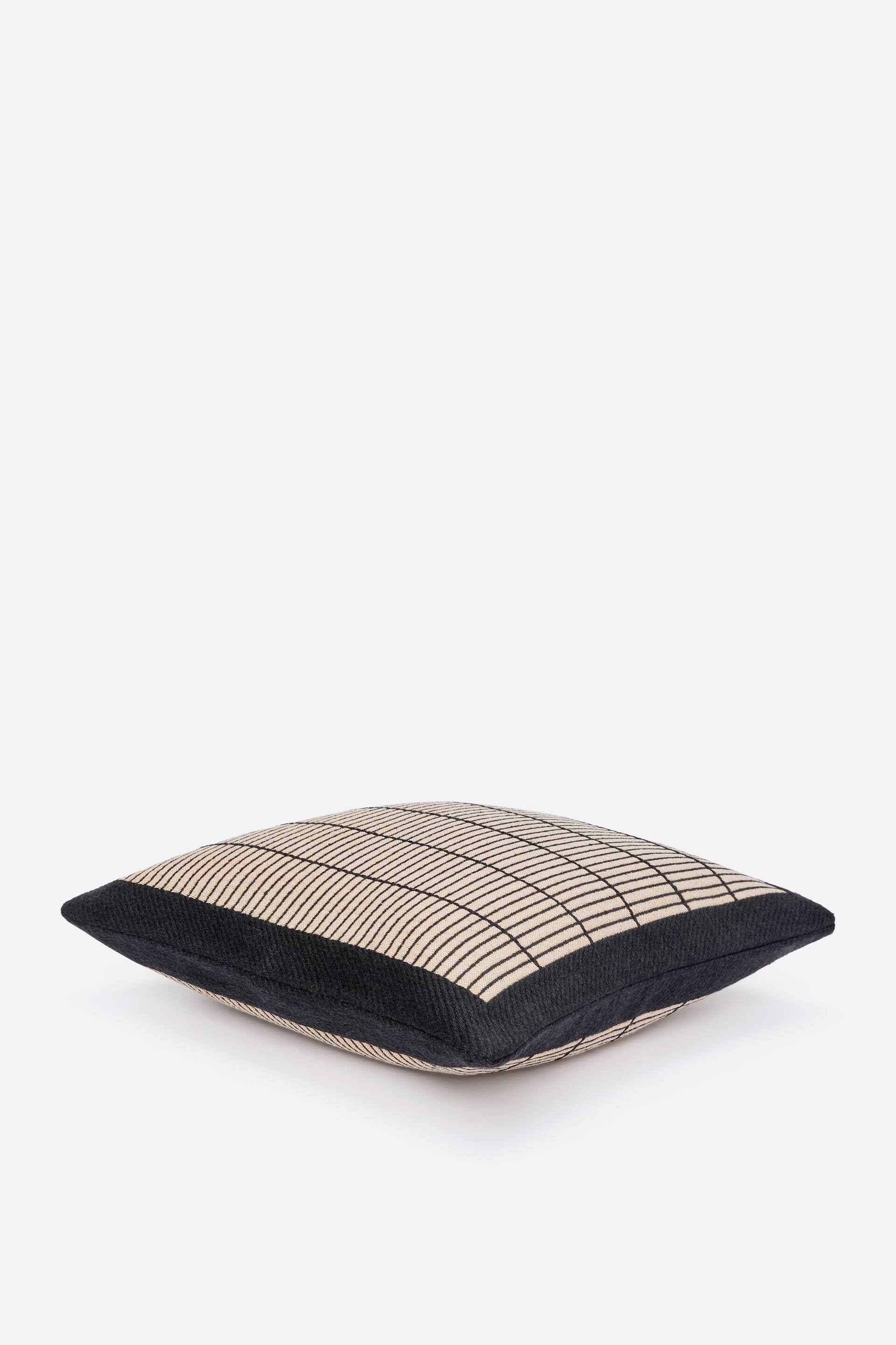 Visa större bild: Ett fyrkantigt kuddfodral ligger, med en ljusfärgad toppanel med ett mörkt rutmönster och solida mörka sidopaneler.
