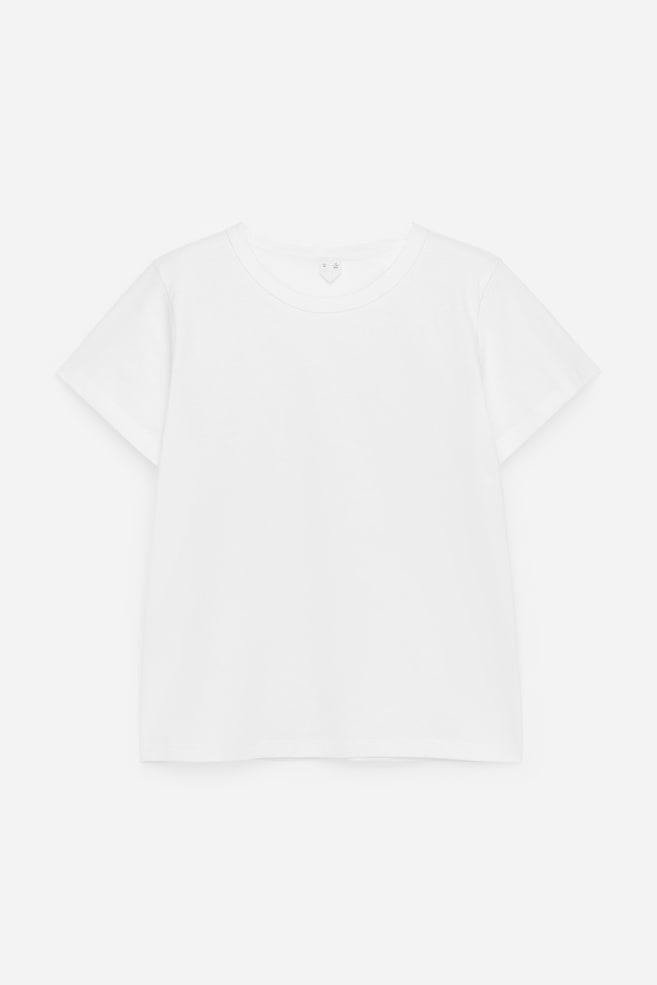 Una camiseta blanca está colocada plana, mostrando su vista frontal. Presenta un cuello redondo y mangas cortas. - 1