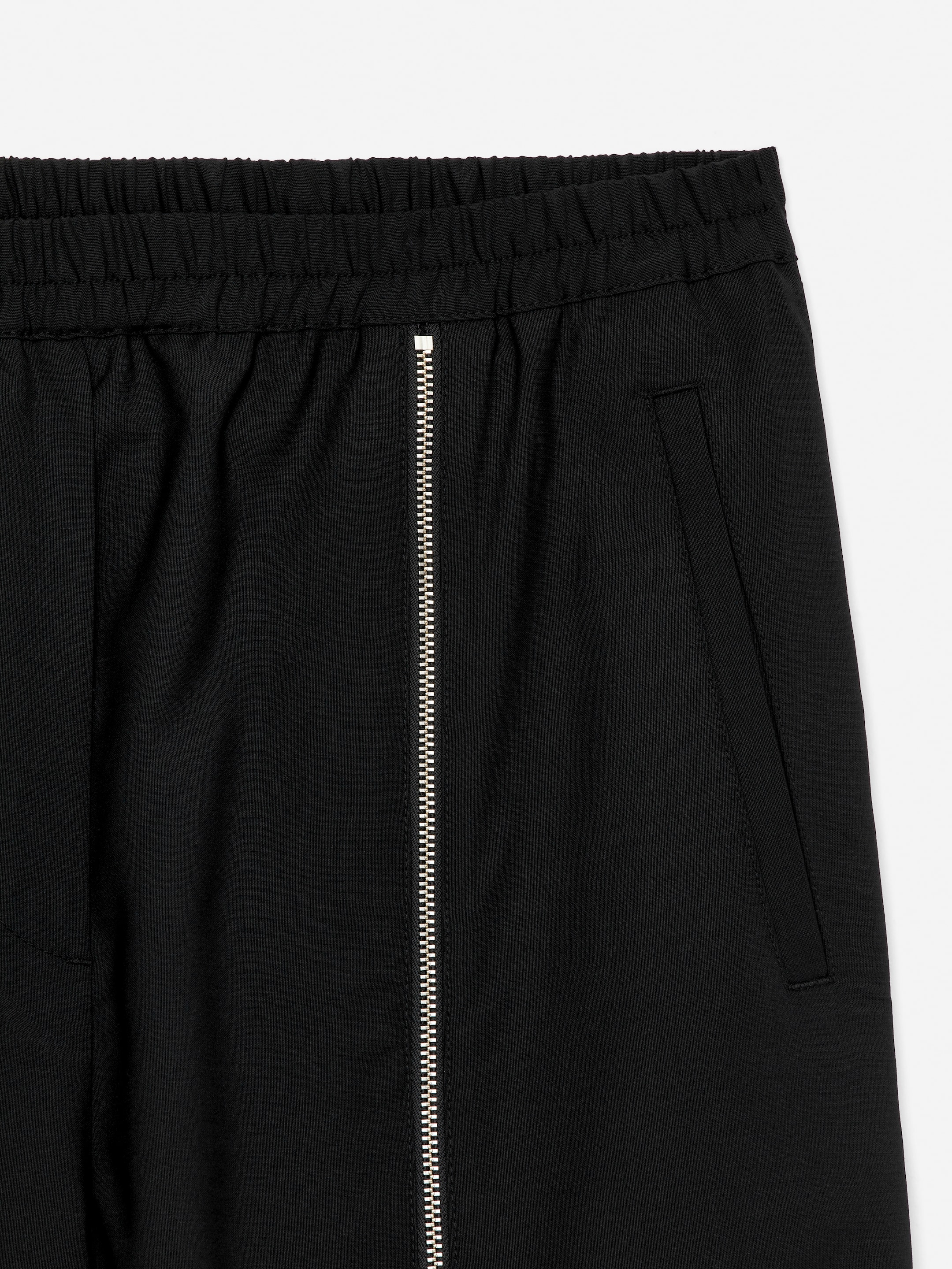 Visualizza immagine più grande: I pantaloni della tuta neri su misura sono presentati dalla parte anteriore, con una vita elasticizzata. Una lunga cerniera verticale argentata corre lungo la gamba dalla cintura, e una tasca laterale a filetto è visibile sul lato destro di chi li indossa.