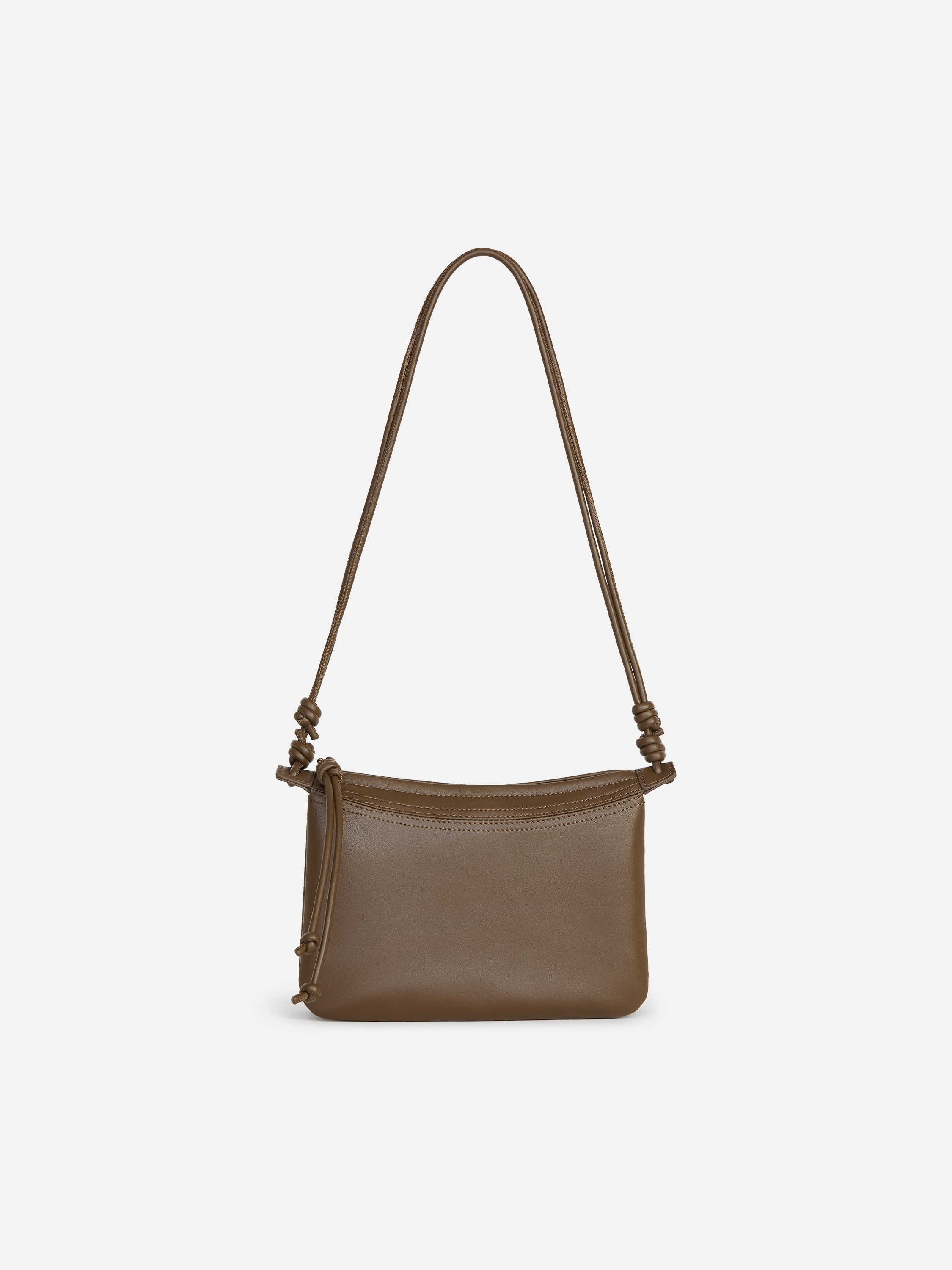 Eine olivgrÃ¼ne Leder-Crossbody-Tasche mit weichem, rechteckigem Beuteldesign und seitlichem Knoten-Detail wird vom Model gehalten. Die Tasche wird in einer Hand getragen, wÃ¤hrend der dÃ¼nne Lederriemen locker an einem dunklen, zweireihigen Mantel herabhÃ¤ngt.