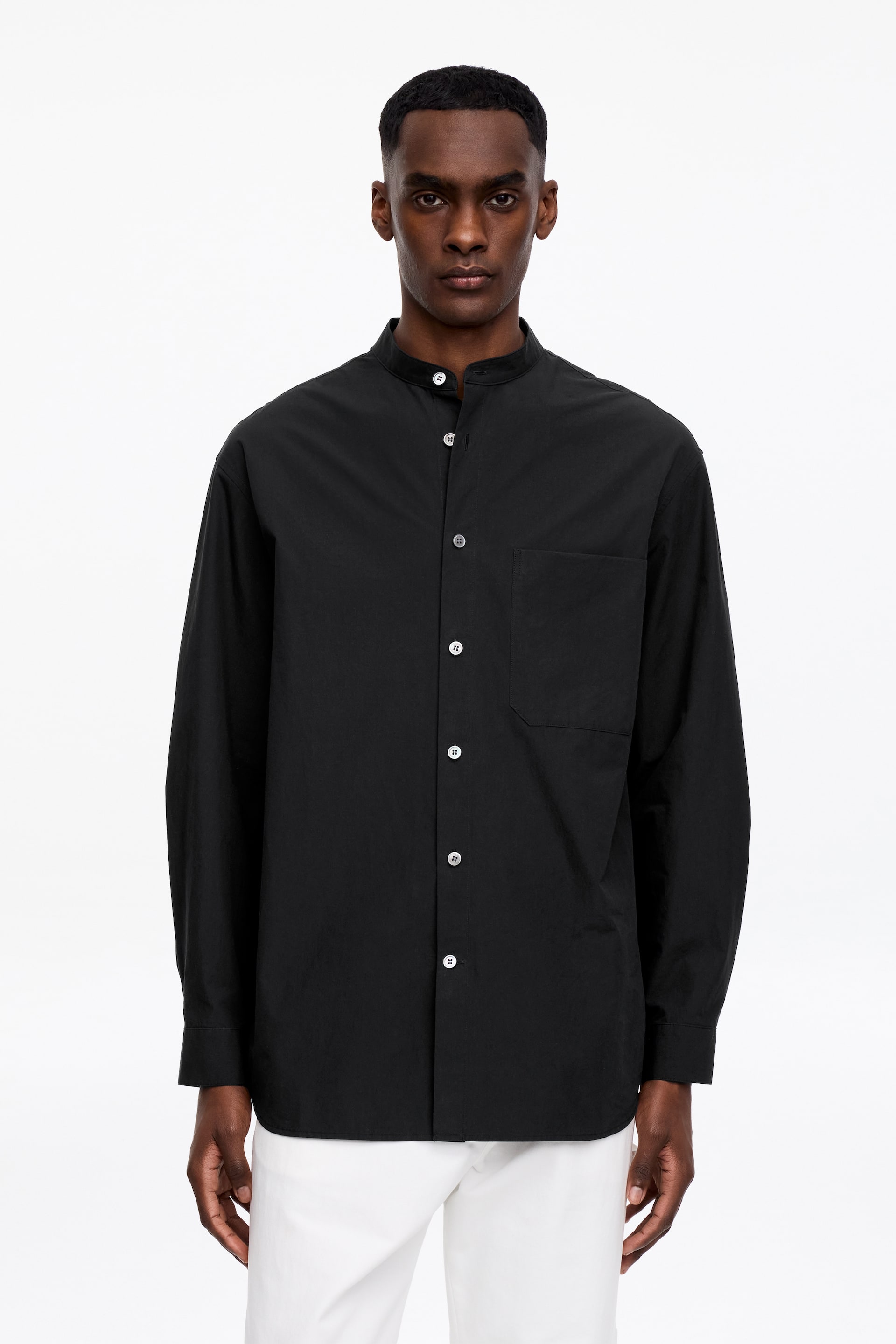 Größeres Bild anzeigen: Ein schwarzes Langarmhemd mit Stehkragen, einer Knopfleiste vorne mit weißen Knöpfen, einer aufgesetzten Brusttasche links und Knopfmanschetten.