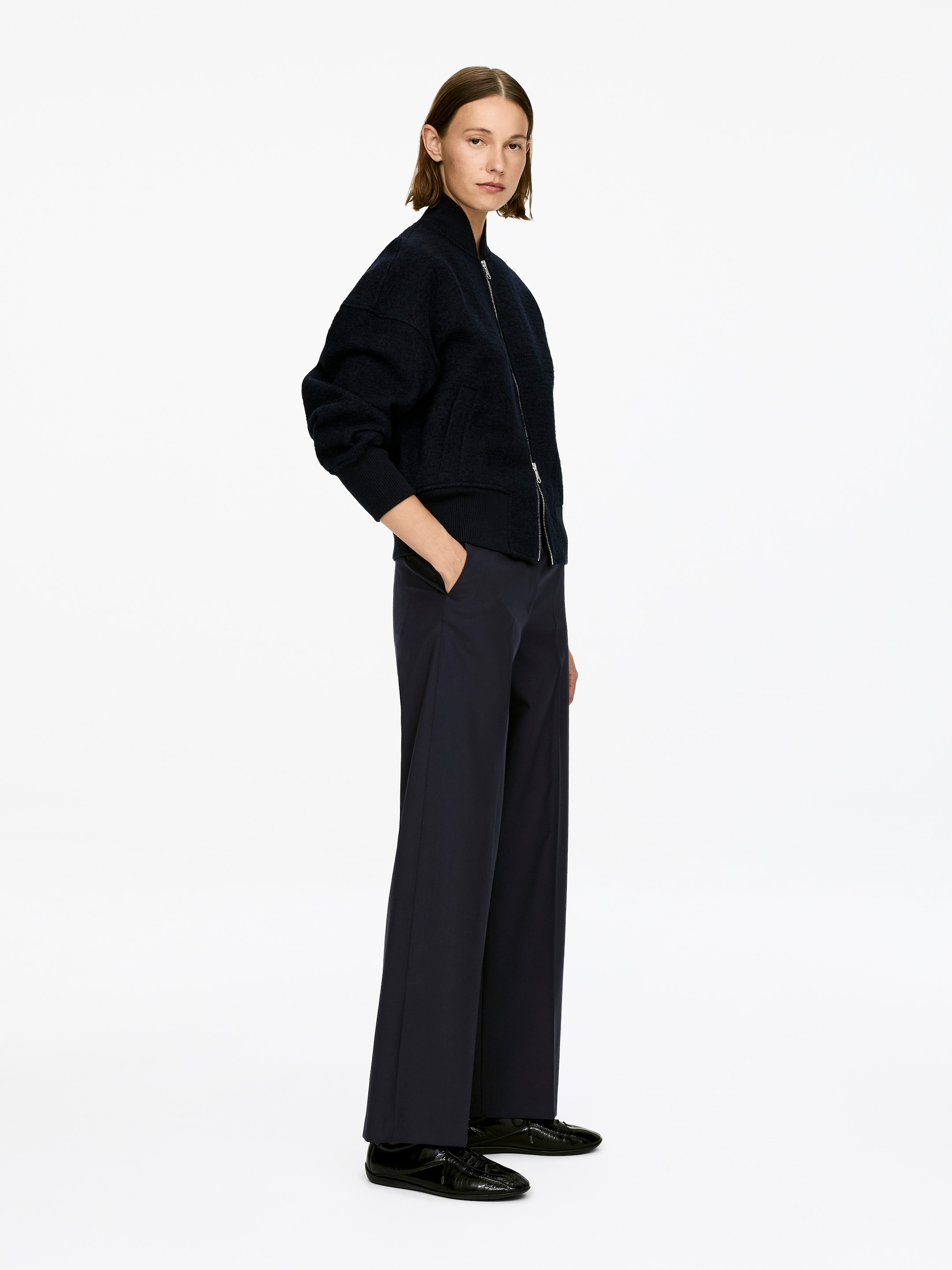 Agrandir l'image: Pantalon bleu foncé avec des plis marqués à l'avant des jambes droites. Le mannequin porte le pantalon taille mi-haute, avec une main reposant dans une poche latérale.