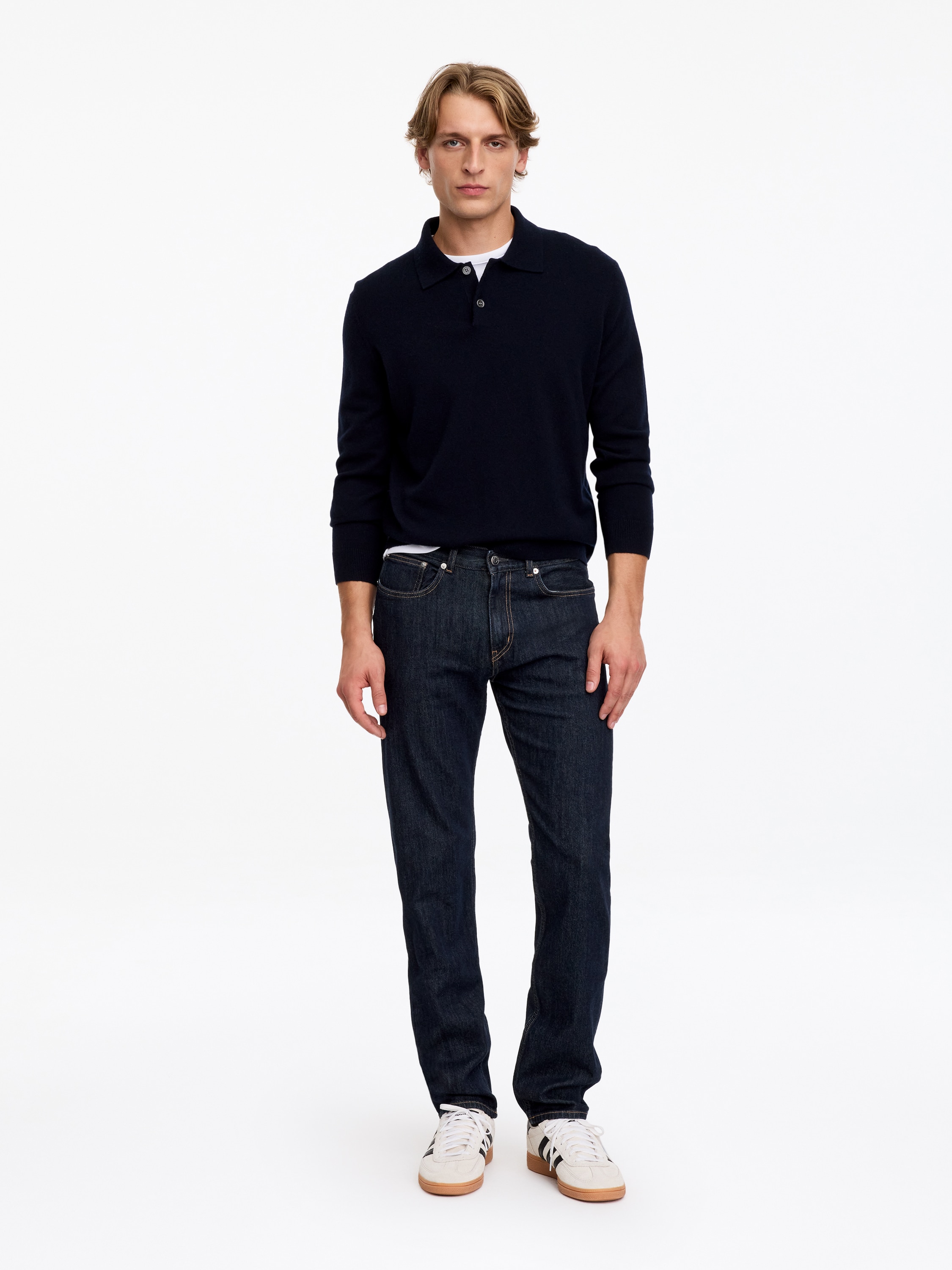 A pair of dark-wash denim jeans is facing forwards, featuring a classic five-pocket design with orange contrast stitching and metal rivets. The jeans have a straight-leg silhouette, a waistband with belt loops, and a single metal button fastening at the centre.