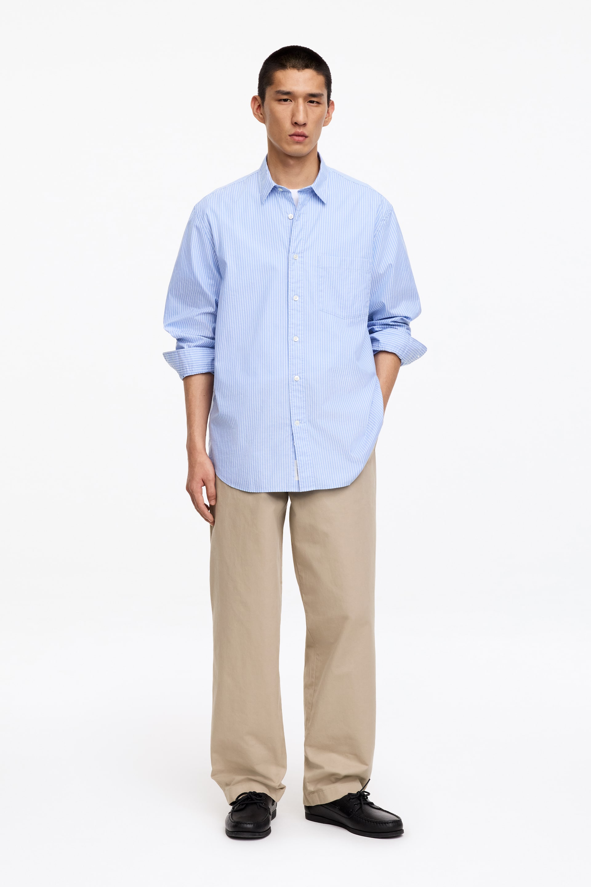 Grotere afbeelding bekijken: Beige wide-fit workwear chino's, met schuine voorzakken en brede riemlussen, worden gedragen door het model.
