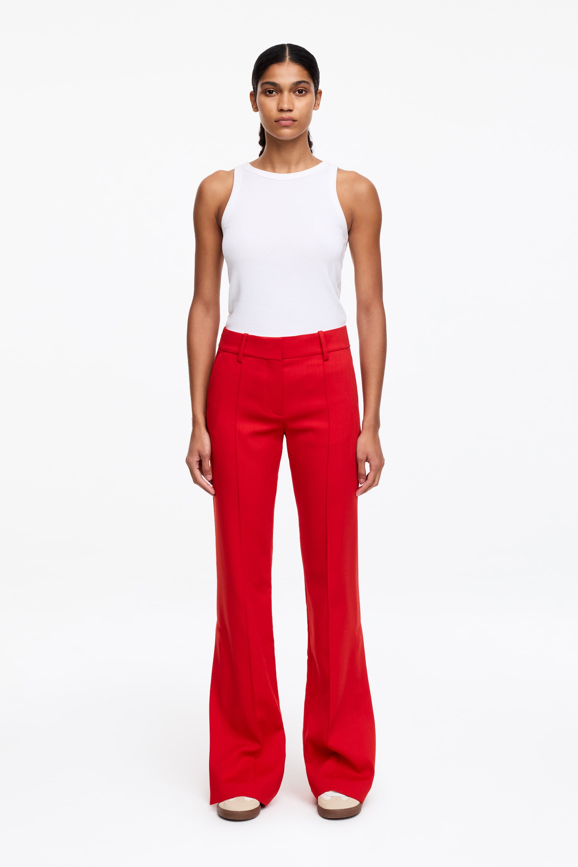 Visa större bild: Röda utsvängda byxor visas framifrån, med ett platt midjeband med bältesöglor och en vertikal framsöm på varje ben. En vit ribbad tanktopp bärs instoppad i byxorna.