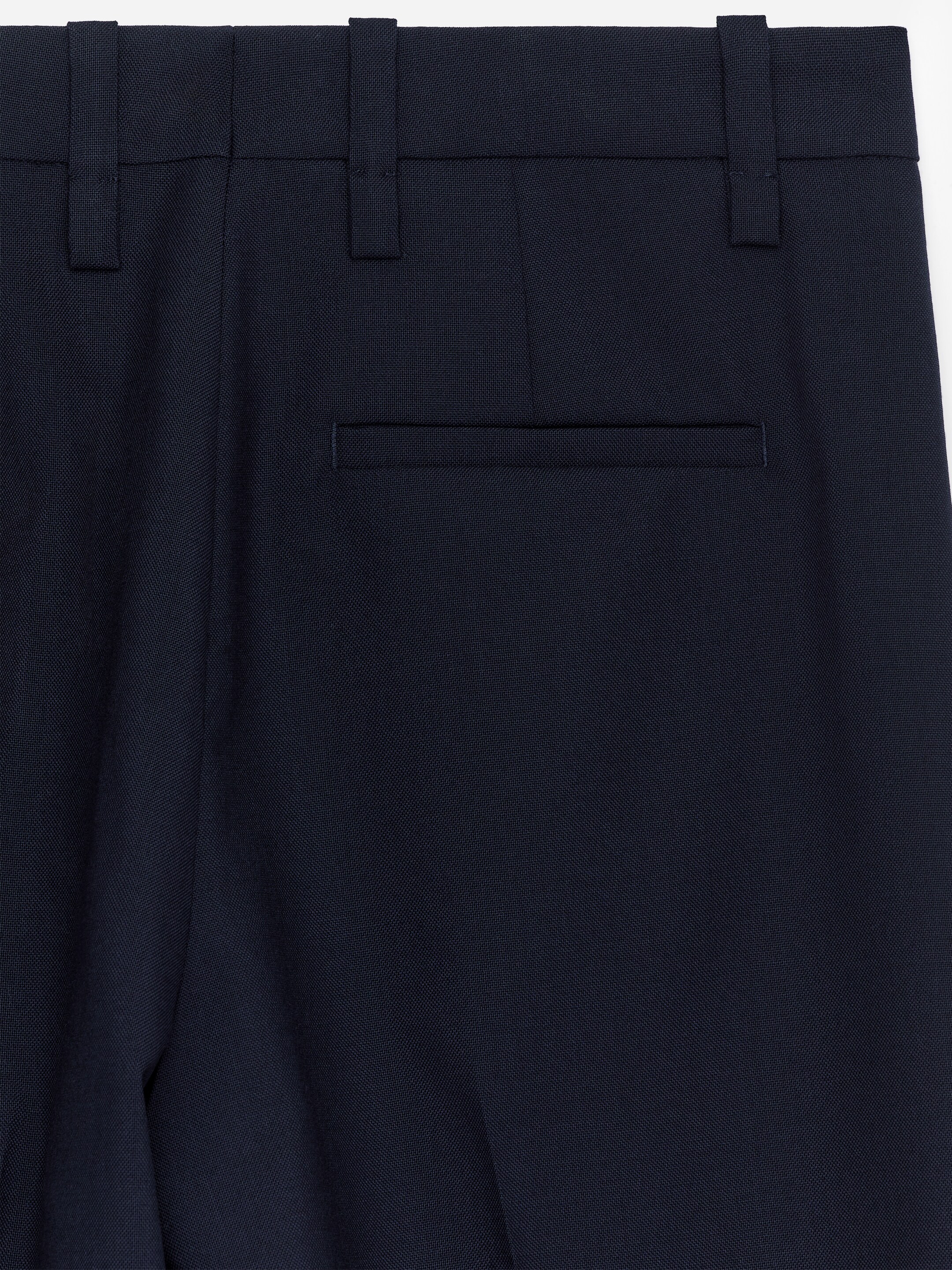 Agrandir l'image: Un pantalon, vu de l'ARRIÈRE, est confectionné avec un tissage hopsack bleu foncé, comportant une seule poche passepoilée horizontale à l'arrière, des passants de ceinture le long de la taille, et un pli discret descendant le long de la jambe.