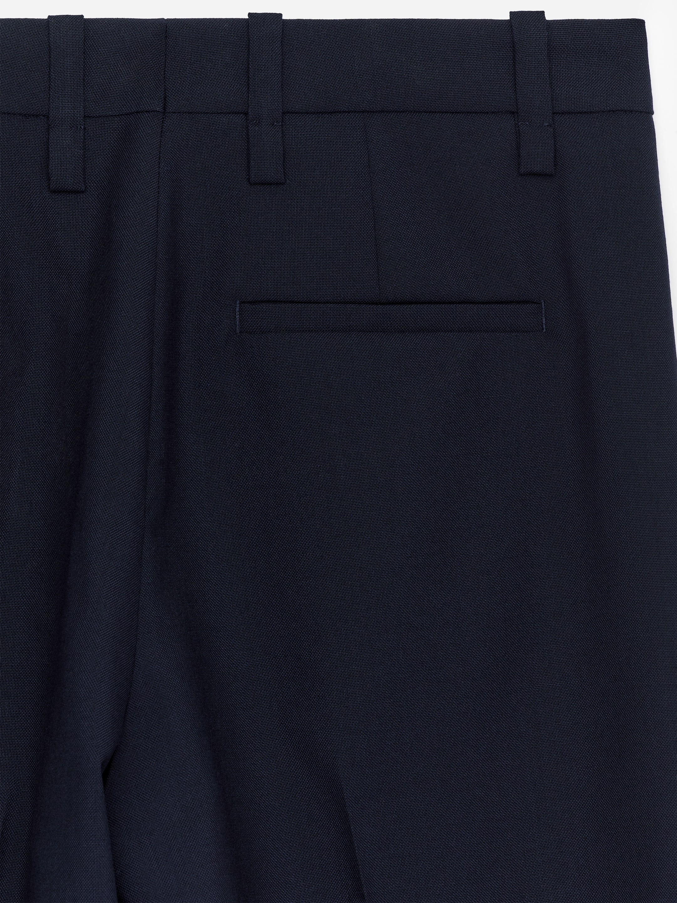 Agrandir l'image: Les pantalons, vus de l'ARRIÈRE, sont confectionnés avec un tissage hopsack bleu foncé, comportant une seule poche passepoilée horizontale à l'arrière, des passants de ceinture le long de la taille, et un pli discret descendant le long de la jambe.