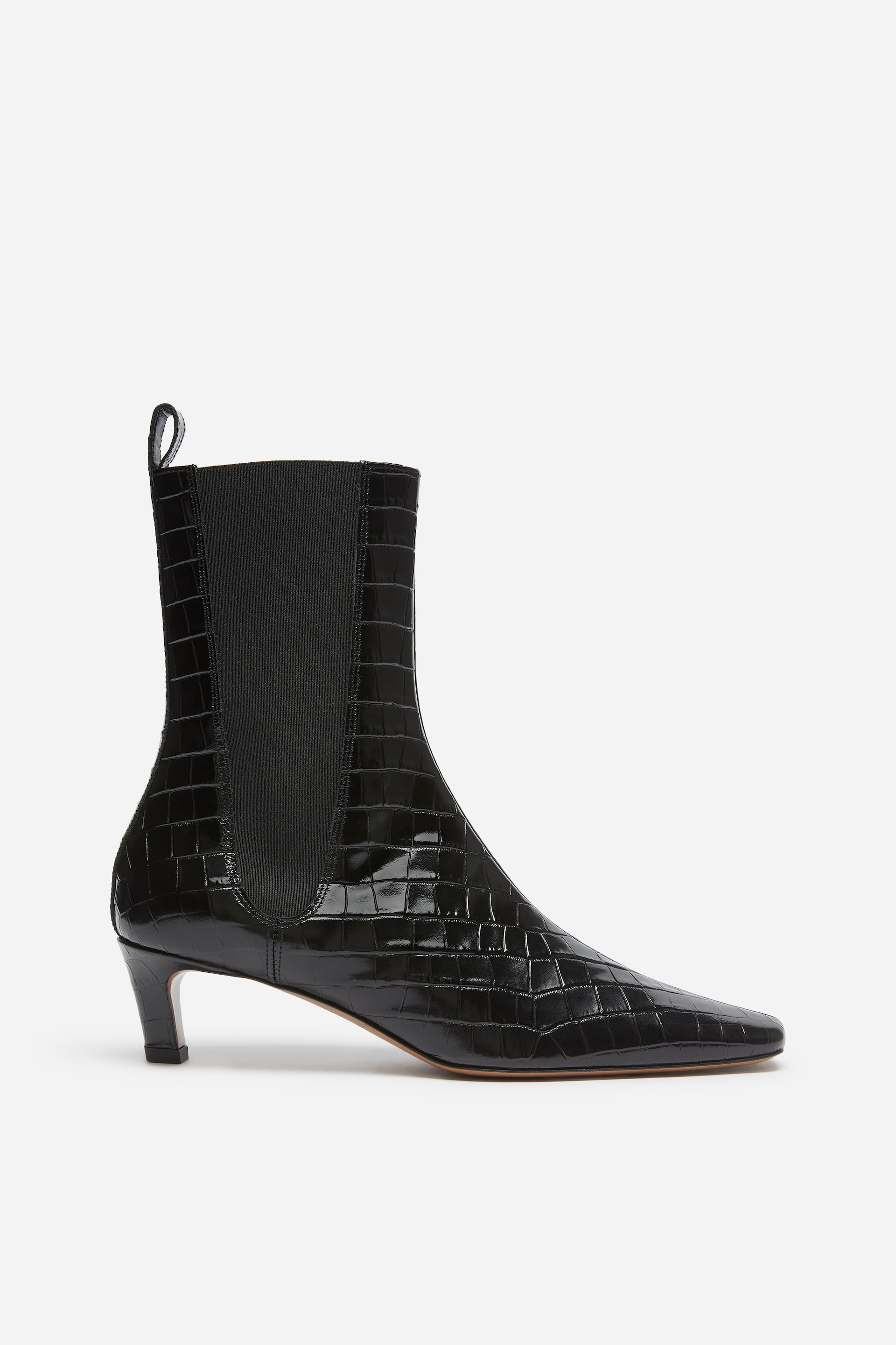View larger image: A black ankle boot is shown in side profile, showcasing a shiny croc-embossed leather finish, an elongated silhouette, and a soft square toe. The boot features a low kitten heel, a black elasticated side panel, and a matching pull tab at the back collar.