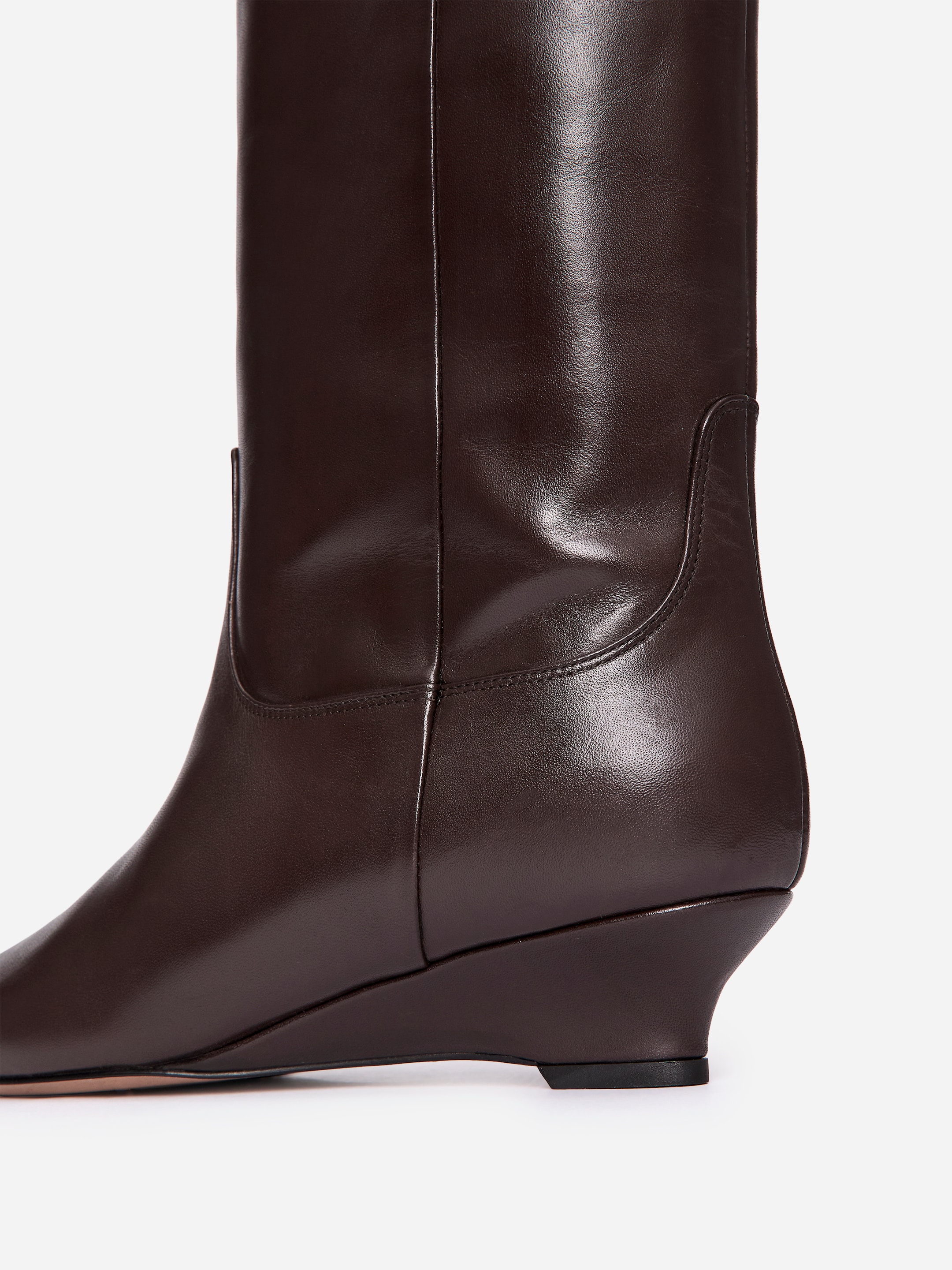 Agrandir l'image: Une botte en cuir brun foncé affiche son profil latéral droit, avec un bout pointu et un talon compensé brun foncé sans couture. La tige haute présente une couture verticale qui remonte le côté et un détail de panneau en forme de U au-dessus du contrefort du talon.