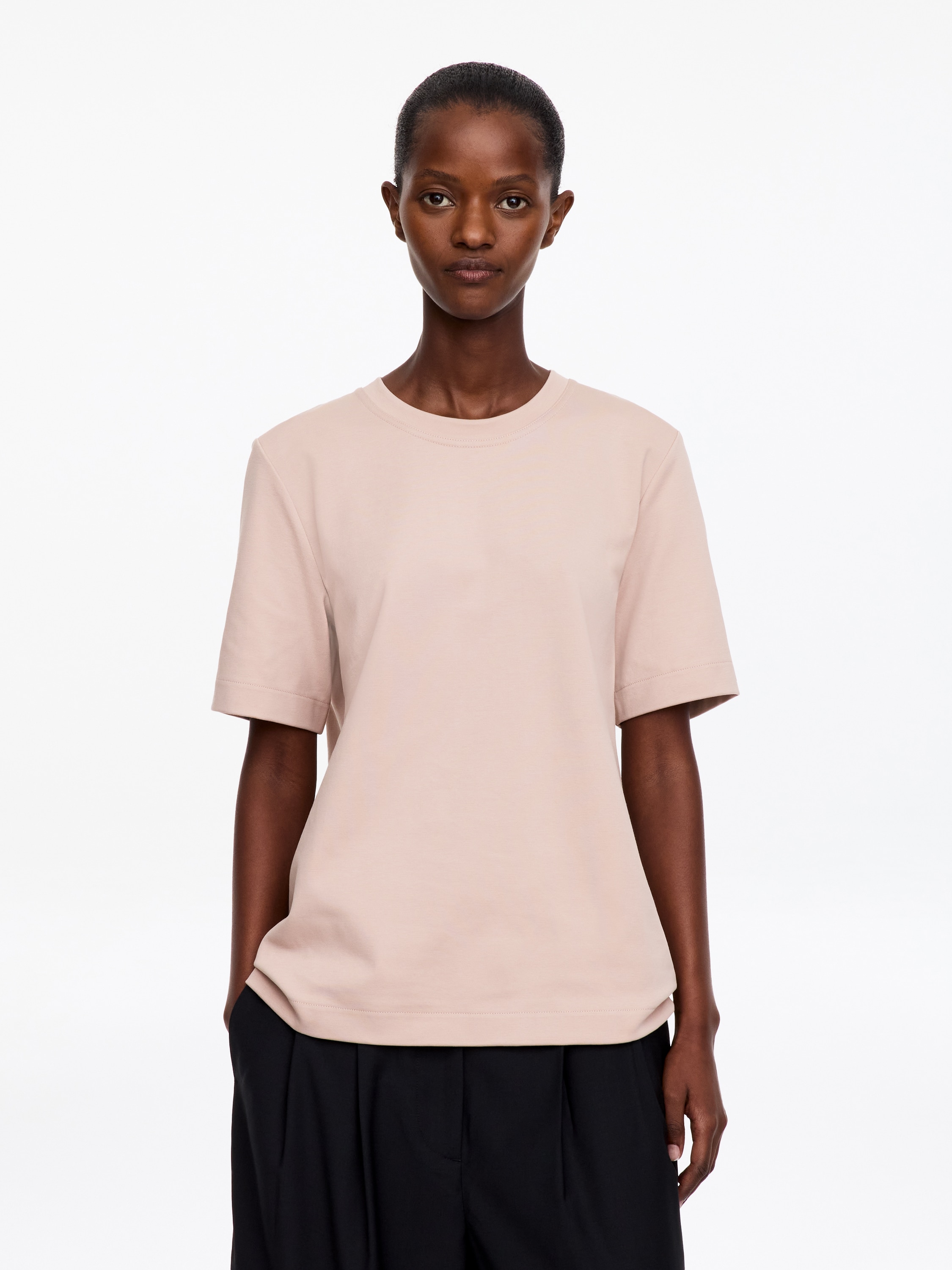 Una T-shirt in jersey di cotone rosa tenue Ã¨ mostrata frontalmente, con classico girocollo a costine, maniche corte e fondo diritto. Il capo presenta una texture liscia e consistente, con una silhouette minimalista a vestibilitÃ  regolare.