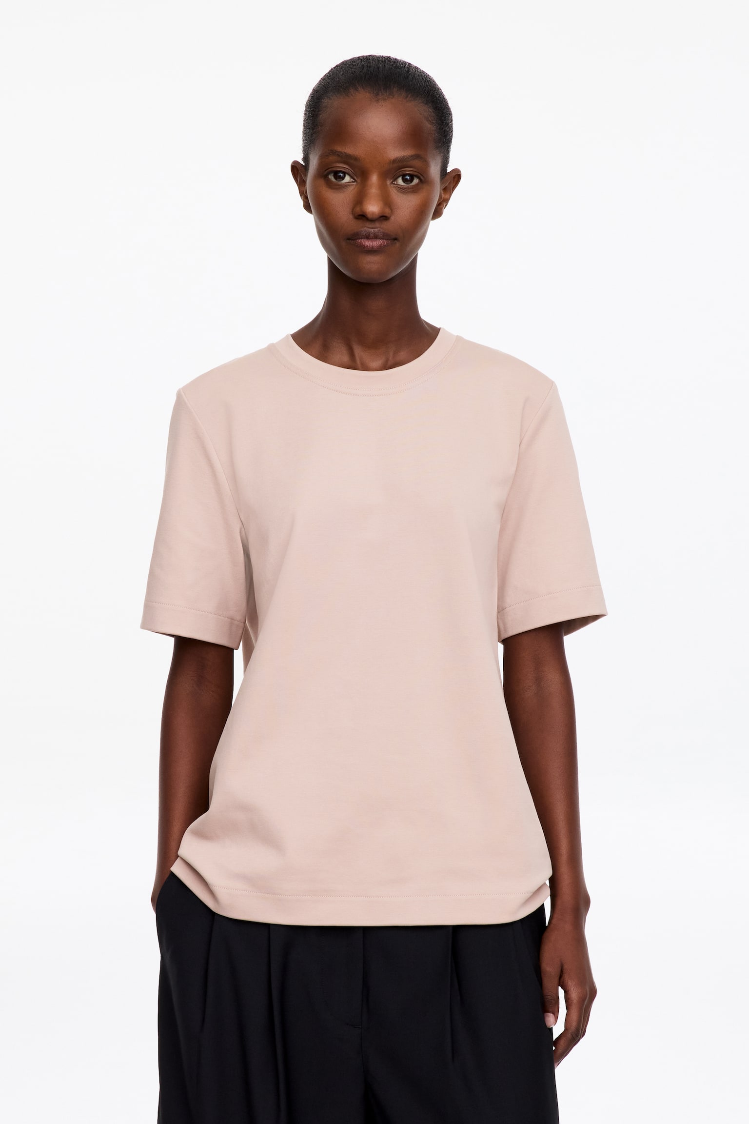Se muestra desde el frente una camiseta de punto de algodón rosa pálido, con clásico cuello redondo acanalado, mangas cortas y bajo recto. La prenda presenta una textura suave y consistente, con una silueta minimalista de corte regular. - 1