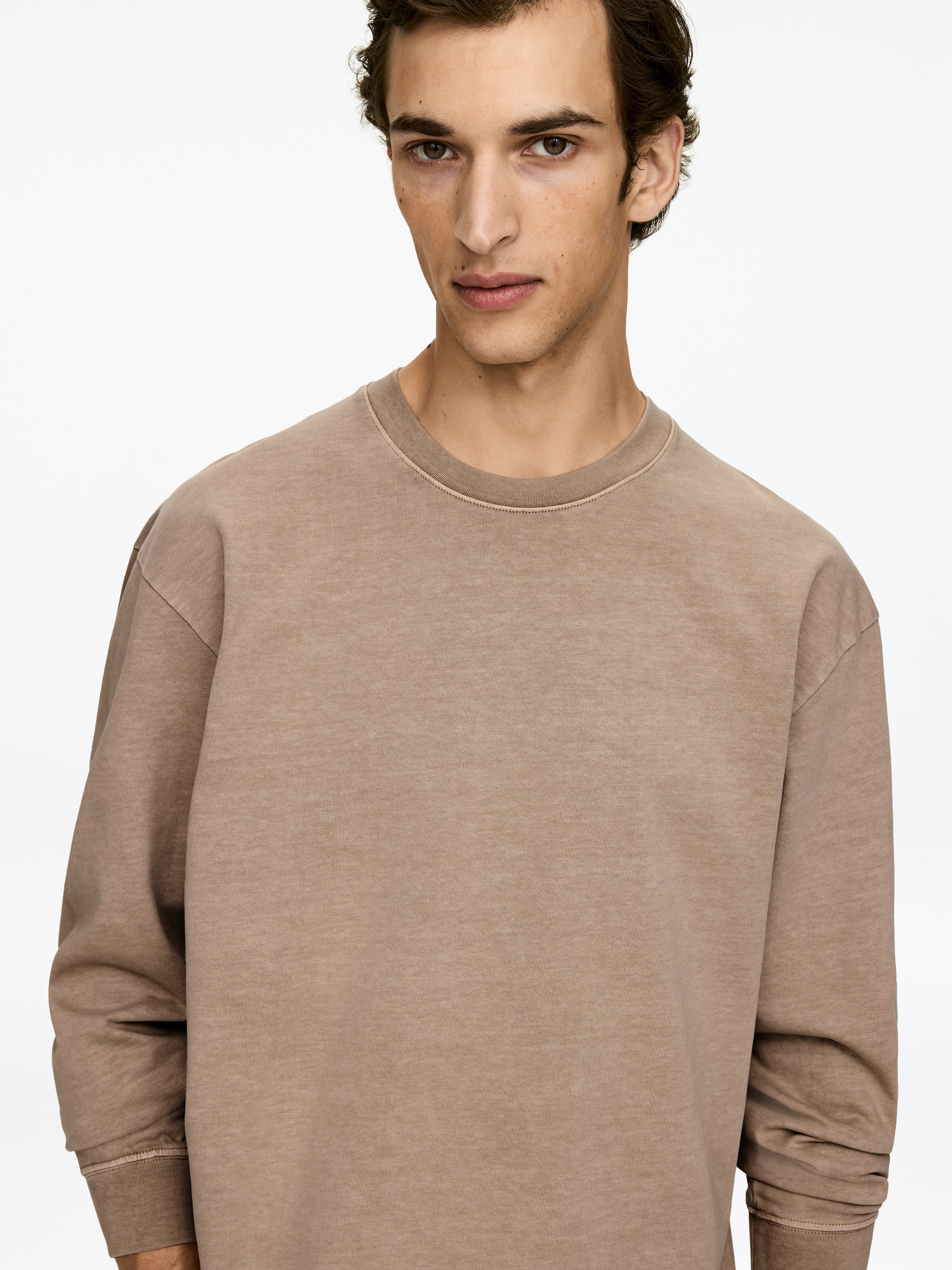 Agrandir l'image: Un sweatshirt brun à col rond lavé est présenté de face sous un angle légèrement incliné. Il présente une coupe décontractée avec un col rond côtelé et des poignets côtelés.