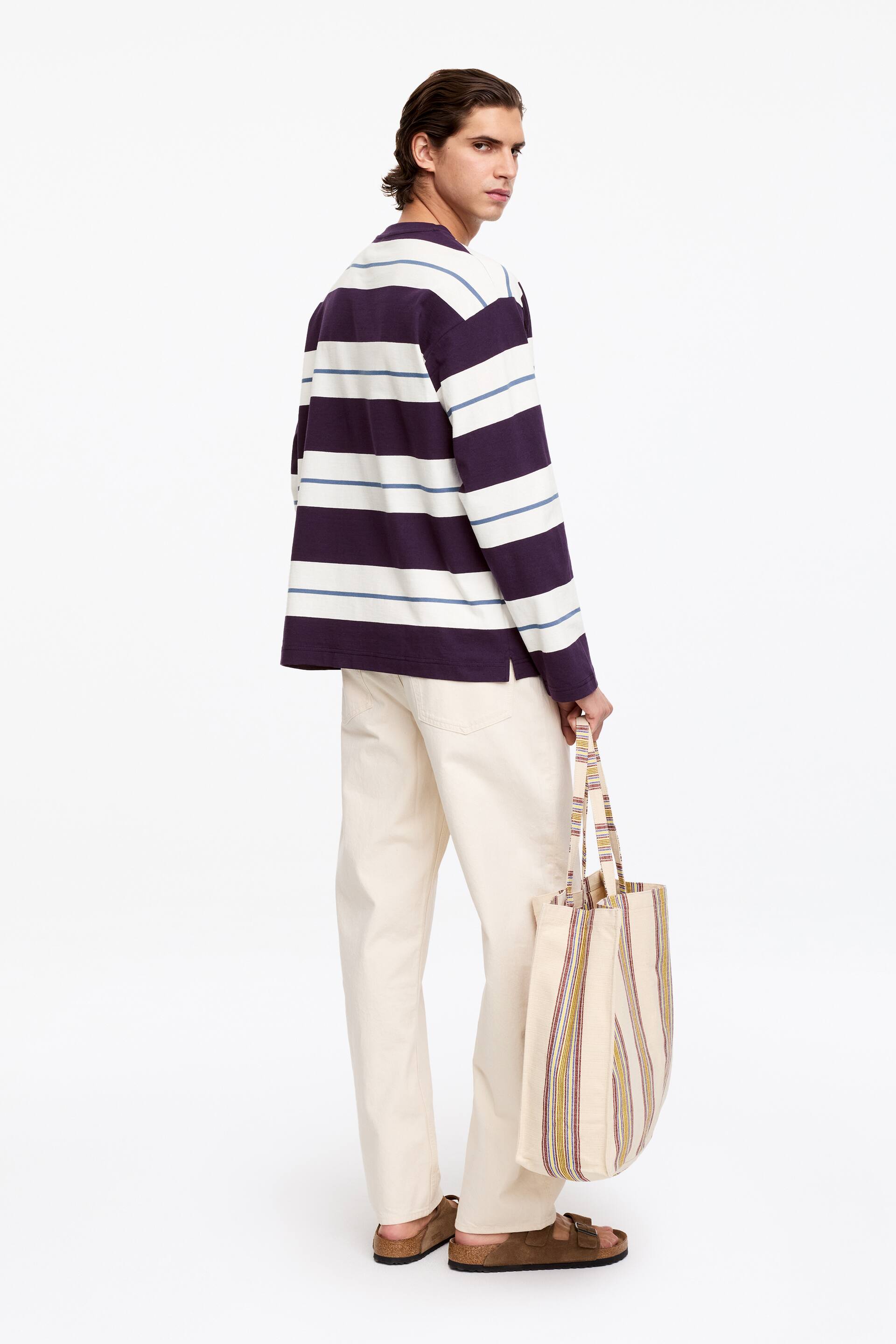 Agrandir l'image: Une chemise de rugby à manches longues avec de larges rayures horizontales en violet, blanc cassé et bleu clair. La chemise est présentée sous un angle de dos, mettant en valeur sa coupe décontractée et le motif complet des rayures.