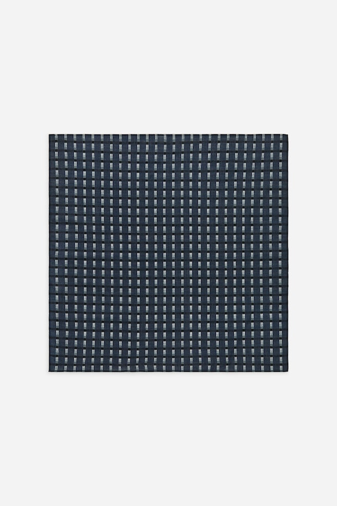 Uma bandana de algodão tecido está estendida, exibindo uma estampa gráfica. A estampa apresenta um fundo azul escuro padronizado com finas linhas horizontais pretas e colunas verticais de pequenos traços claros, formando uma grelha. - 1
