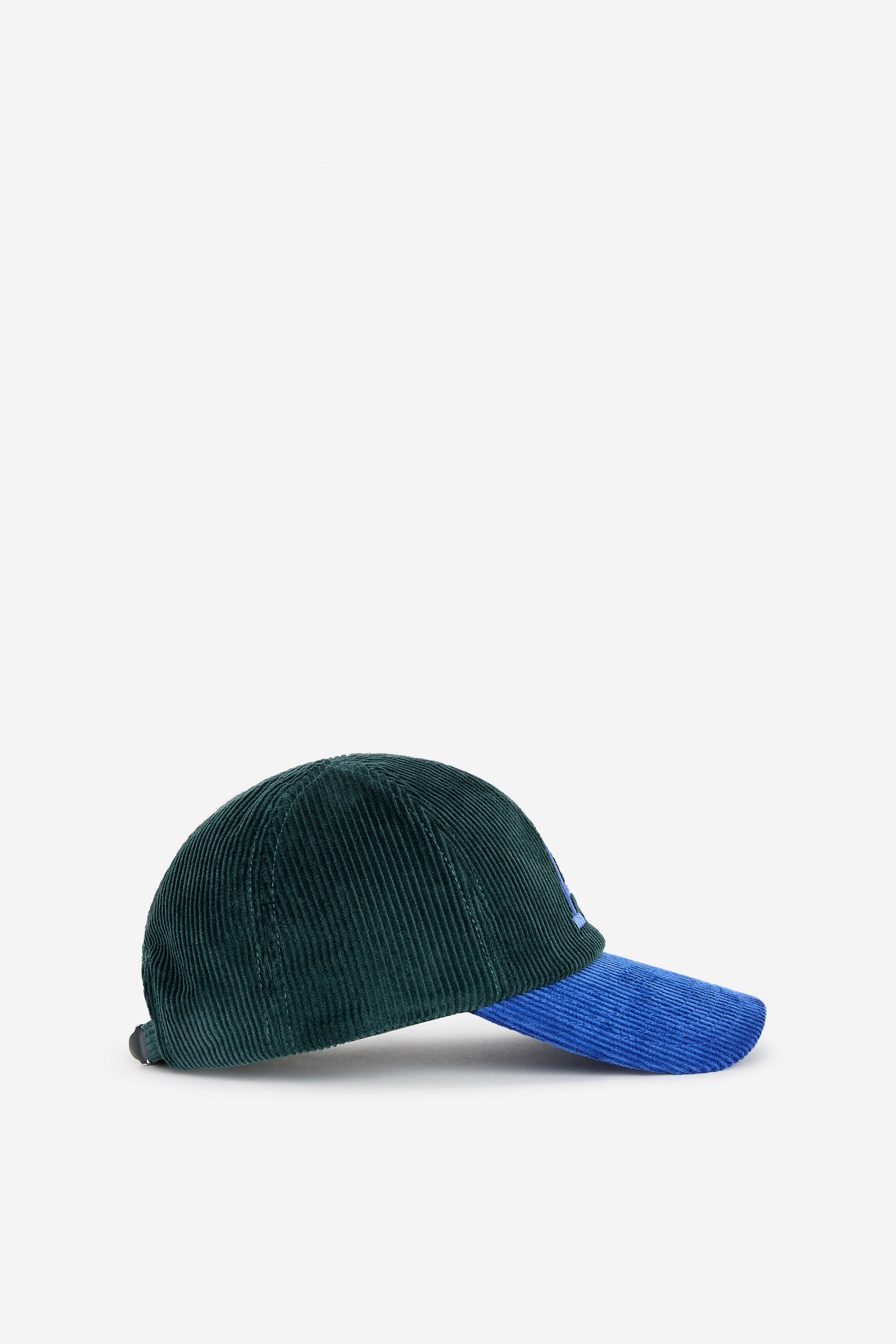 View larger image: A corduroy baseball cap is displayed in a side view, featuring a dark green crown and a blue brim. A blue embroidered design is shown on the side of the crown.