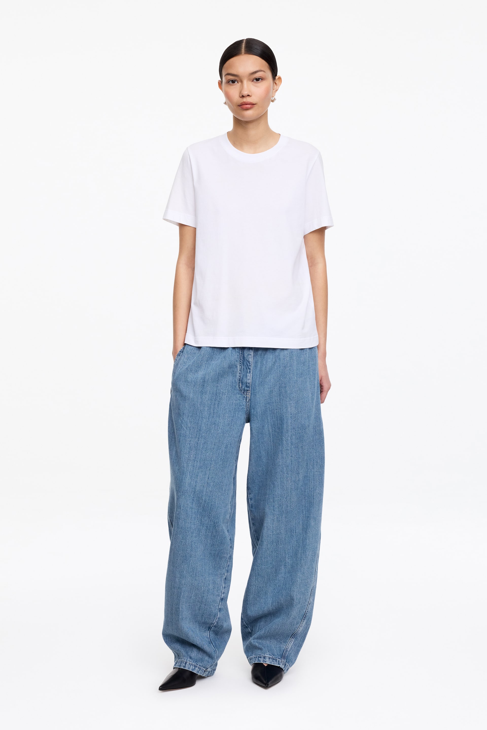 Visualizza immagine più grande: Una t-shirt bianca con scollo a girocollo presenta maniche corte e una vestibilità rilassata e dritta, con una texture liscia e un orlo dritto che cade sui fianchi.