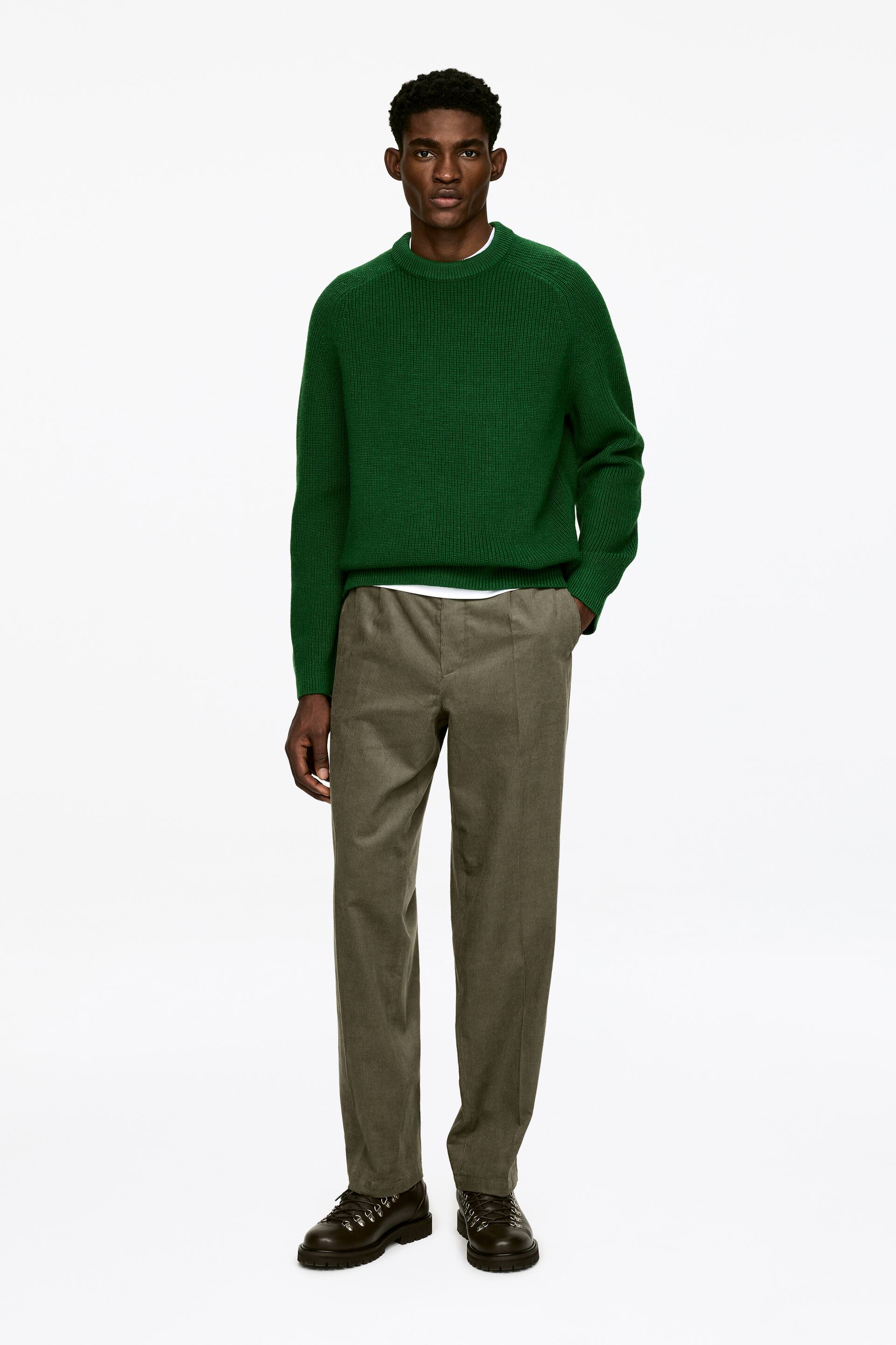 Agrandir l'image: Pantalon en velours côtelé vert olive, avec une coupe décontractée et des jambes droites, porté par le mannequin. Le mannequin glisse une main dans une poche couture latérale.