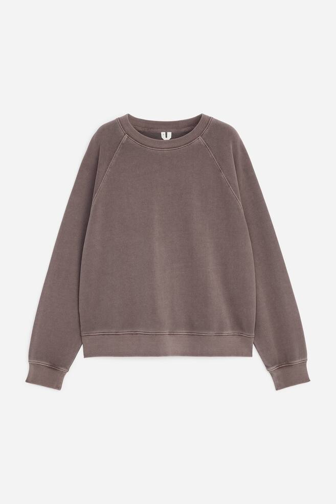 En sweatshirt med rund halsringning i en urtvÃ¤ttad brun nyans visas framifrÃ¥n och framhÃ¤ver de lÃ¥nga raglanÃ¤rmarna samt ribbade detaljer vid kragen, Ã¤rmsluten och fÃ¥llen. Plagget har en mjuk, texturerad yta med synliga sÃ¶mmar lÃ¤ngs sÃ¶mmarna. - 1