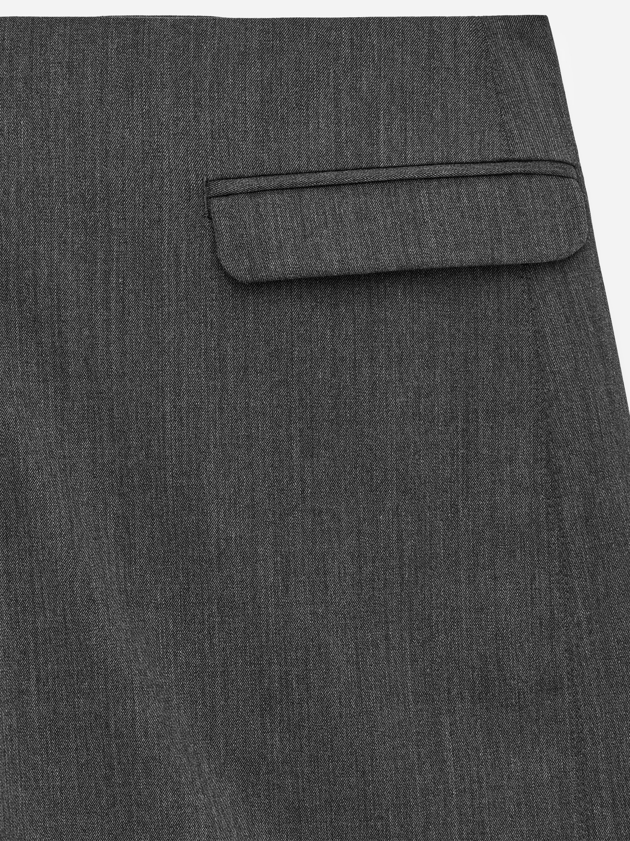 Visualizza immagine più grande: Un indumento grigio scuro presenta una tasca con patta con angoli inferiori arrotondati, posizionata sopra un'apertura orizzontale. Il tessuto presenta una trama fine a twill.