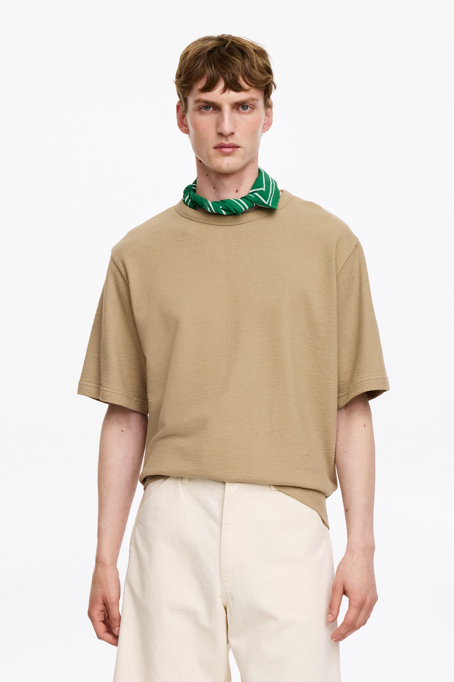 Visualizza immagine più grande: Una t-shirt color sabbia a maniche corte è caratterizzata da un tessuto a maglia testurizzato e da un girocollo. Presenta una vestibilità rilassata con maniche ampie e un orlo dritto non infilato.