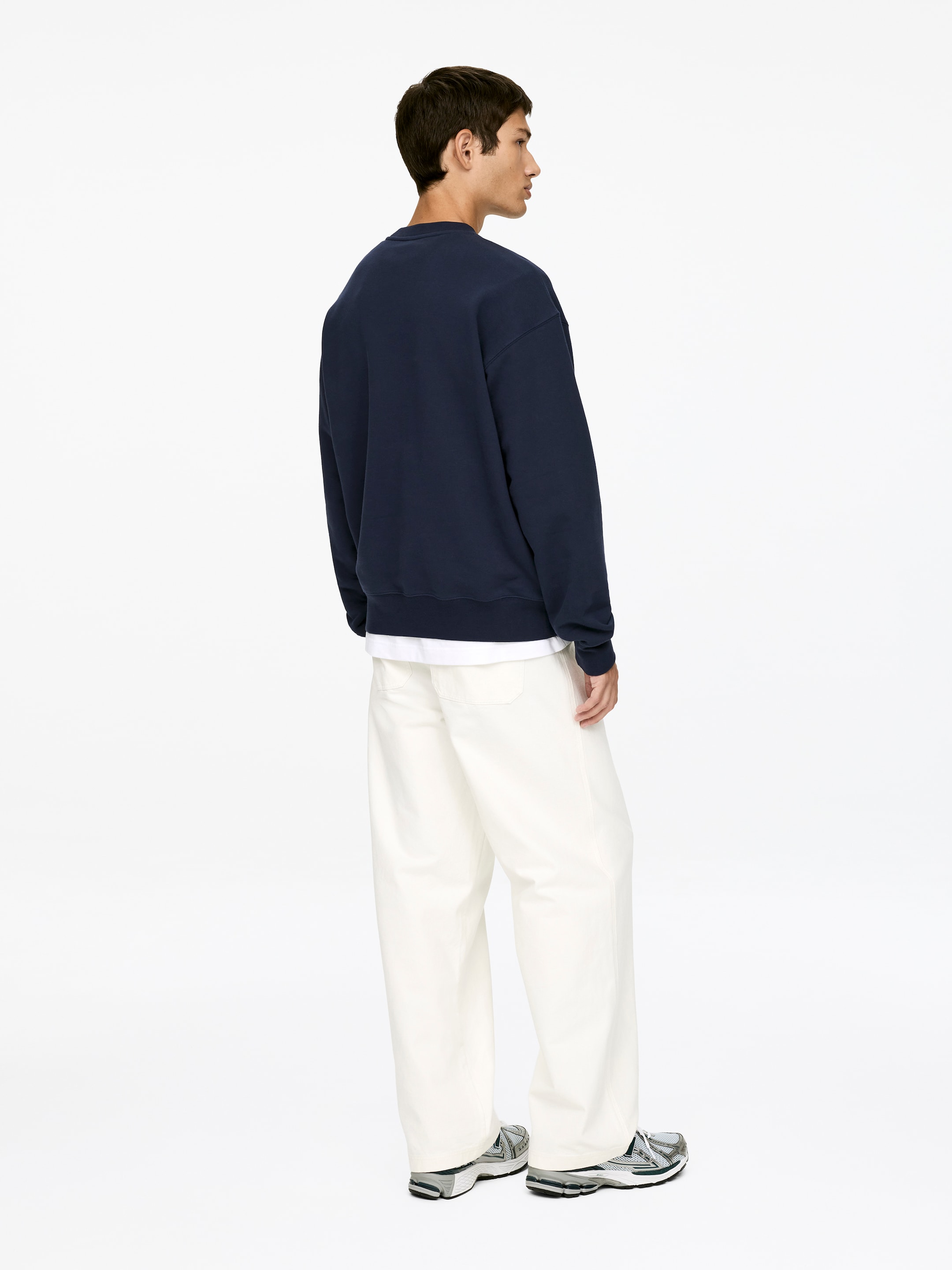 Visa större bild: En marinblå sweatshirt med rund hals presenteras från bak-höger sida och har en avslappnad passform. En vit t-shirt lager under, synlig vid fållen.