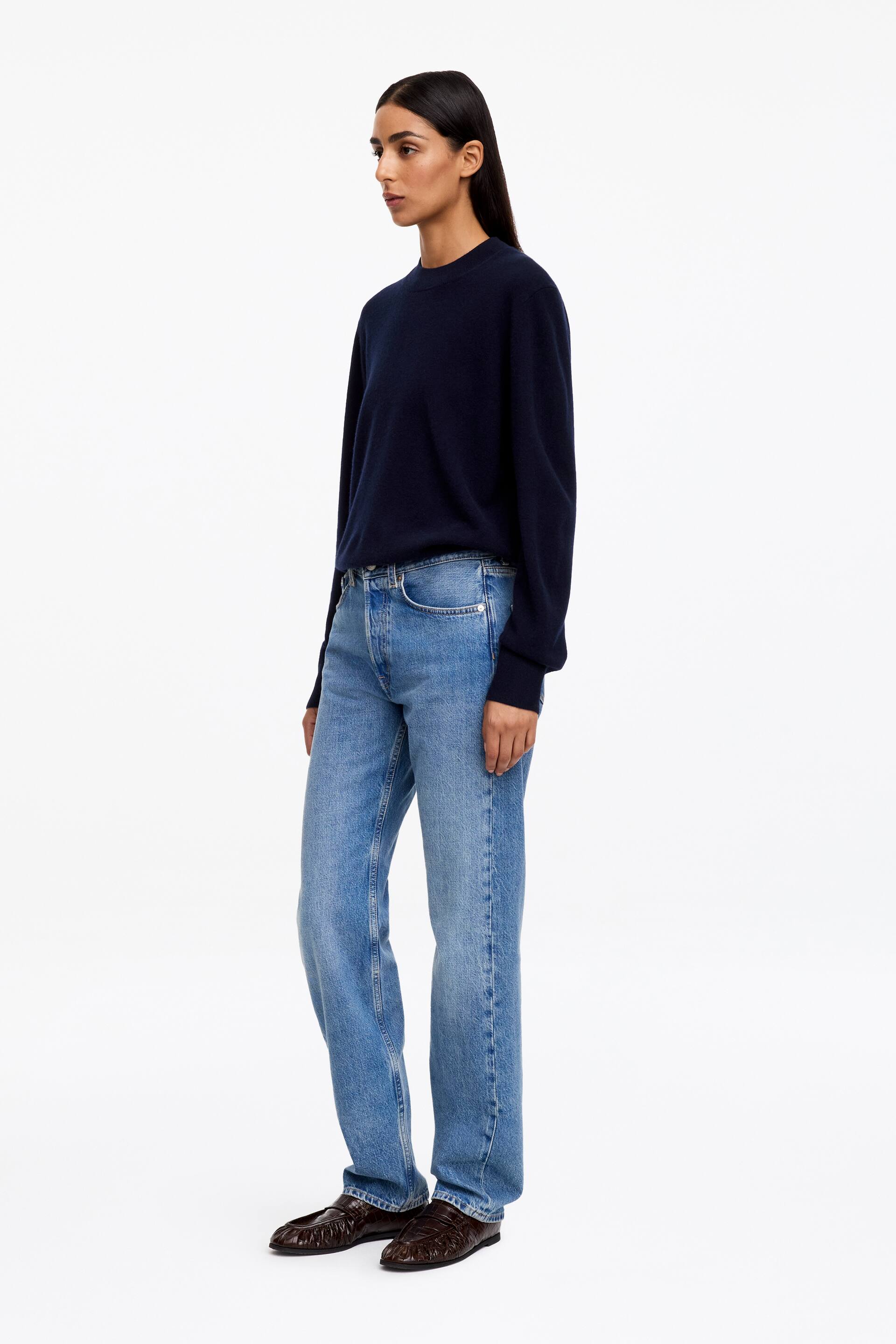 Agrandir l'image: Un pull en maille bleu foncé, à la silhouette épurée, avec col montant factice et finitions côtelées, est porté par le mannequin. Le mannequin l’associe à un jean délavé clair.