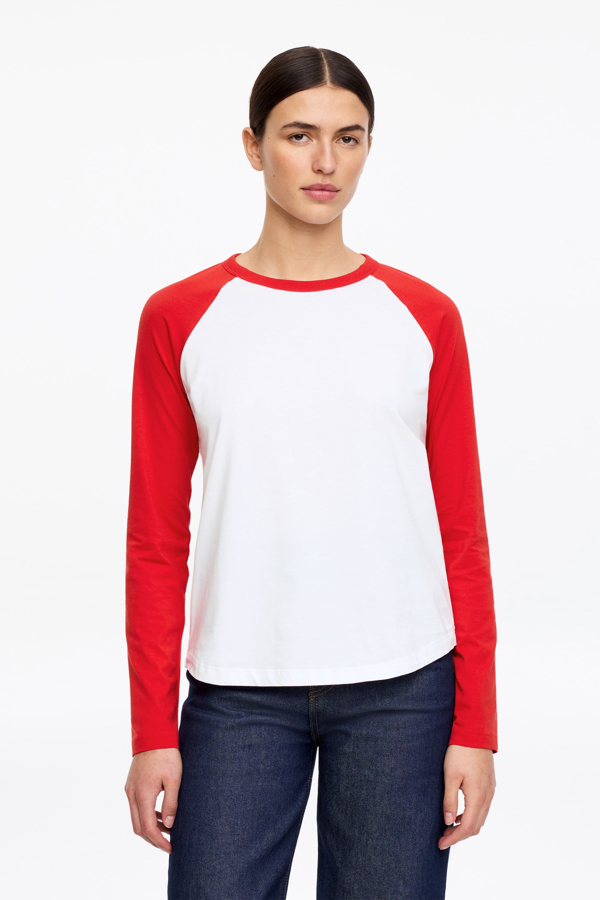 Ingrandisci l'immagine: Una maglietta raglan a maniche lunghe con fronte in vista presenta un corpo bianco e maniche rosse vivaci. È progettata con uno scollo rotondo e un orlo leggermente curvato.