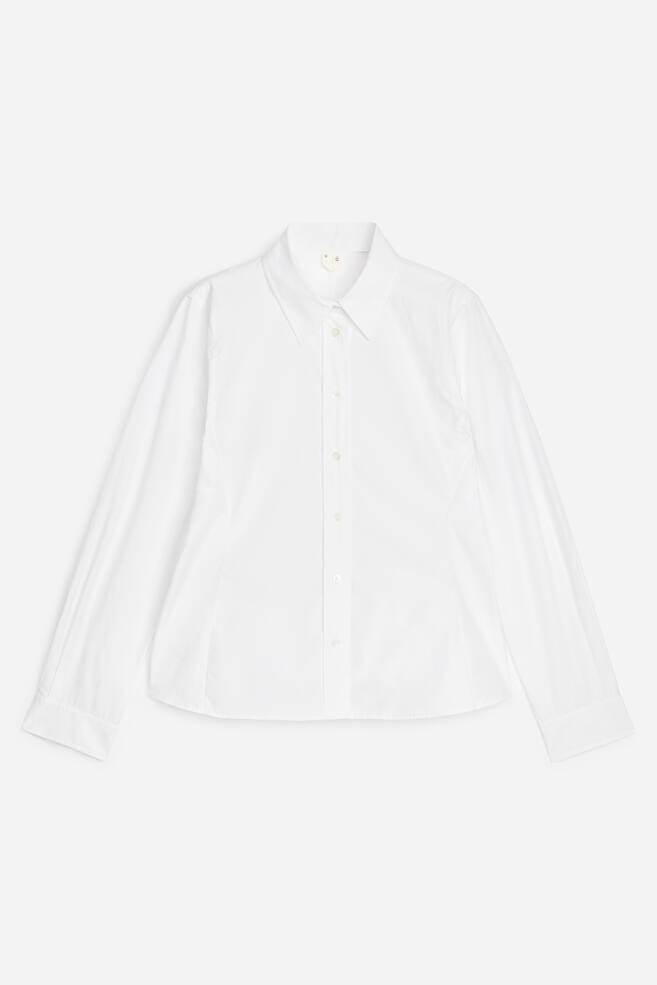 A white long-sleeved shirt is showcasing its front, featuring a classic pointed collar, a full-button placket with light-coloured buttons, and single-button cuffs. The shirt displays a tailored fit with vertical seams along the sides and a curved hem. - 1