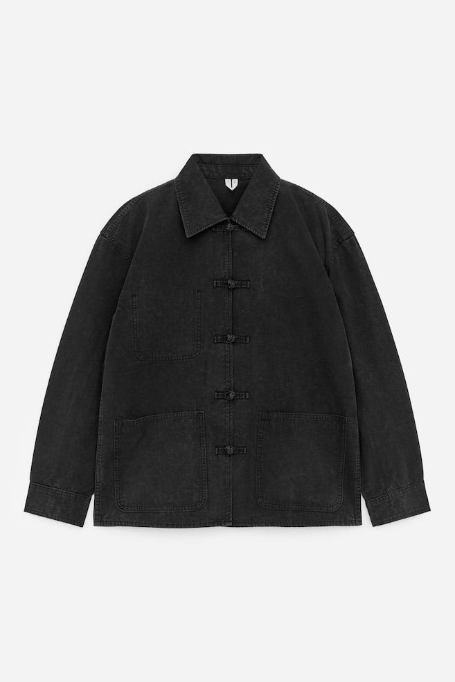 A washed black jacket featuring a spread collar, three frog fastenings down the front, two large patch pockets on the lower front, and long sleeves with straight cuffs. - 1