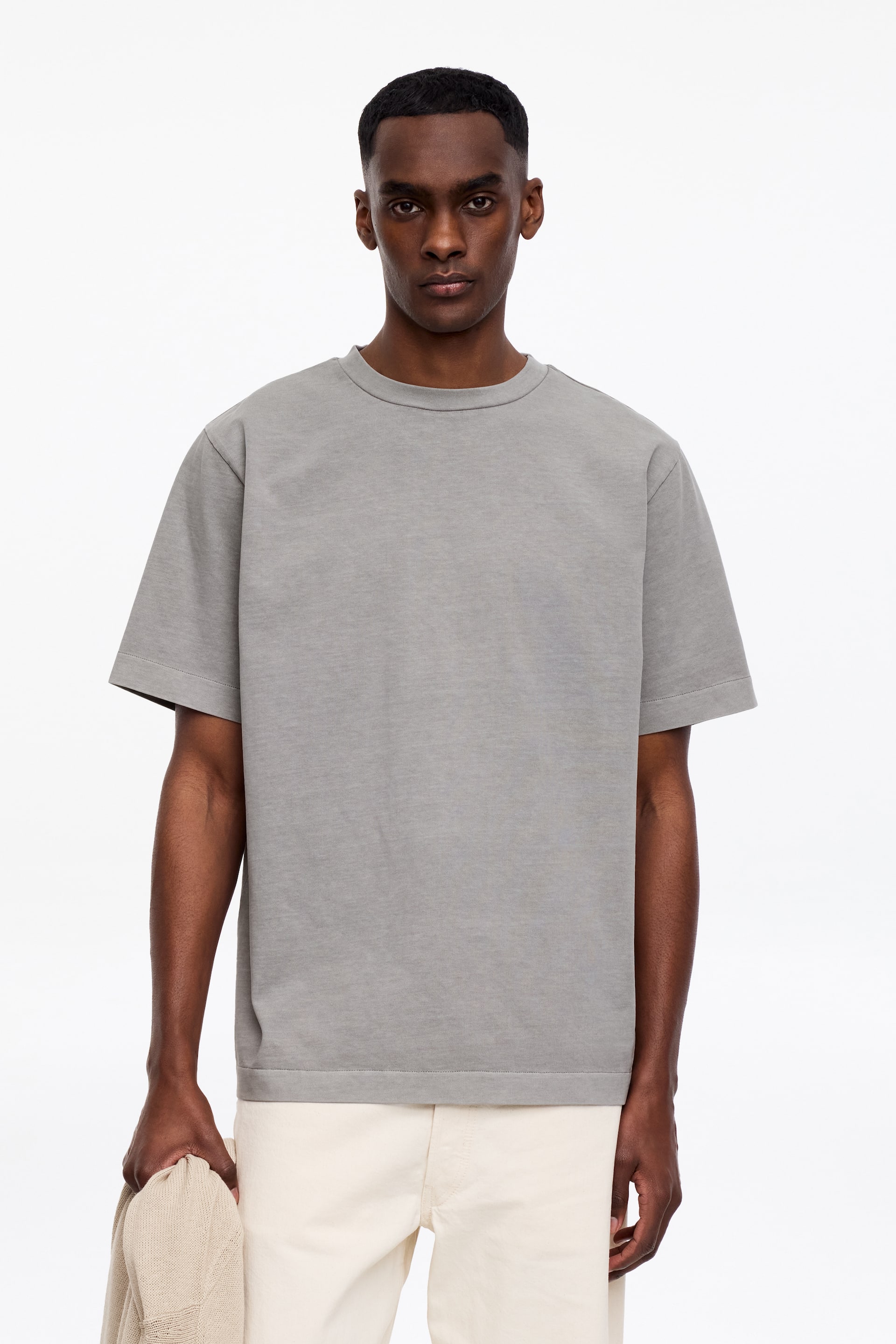 Visa större bild: En grå t-shirt visas framåt, med en rund halsringning och en ribbad krage. Den har en avslappnad passform med korta ärmar och en rak fåll avslutad med ett brett ribbat band.