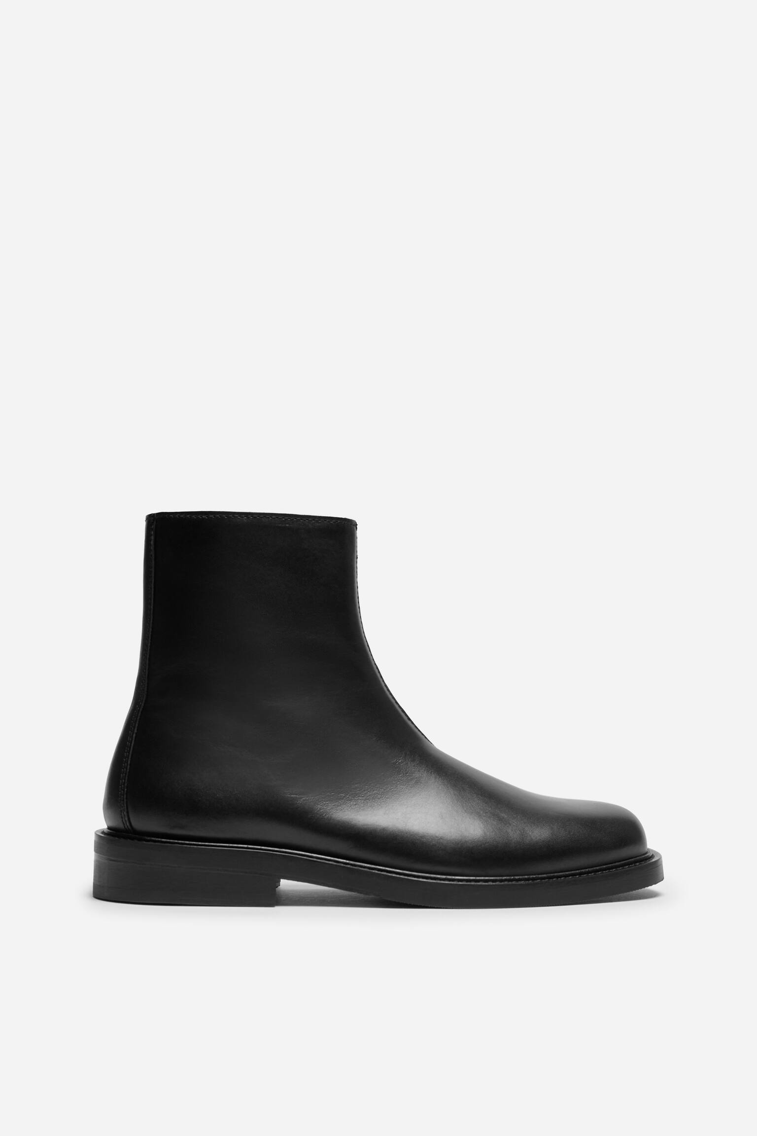 Ein schwarzer Leder-Stiefelette ist in der Seitenansicht zu sehen und prÃ¤sentiert ein glattes Lederobermaterial, eine abgerundete Spitze und einen niedrigen Blockabsatz. Der Stiefel verfÃ¼gt Ã¼ber einen eleganten, strukturierten knÃ¶chelhohen Schaft und eine dicke, flache schwarze Sohle. - 1