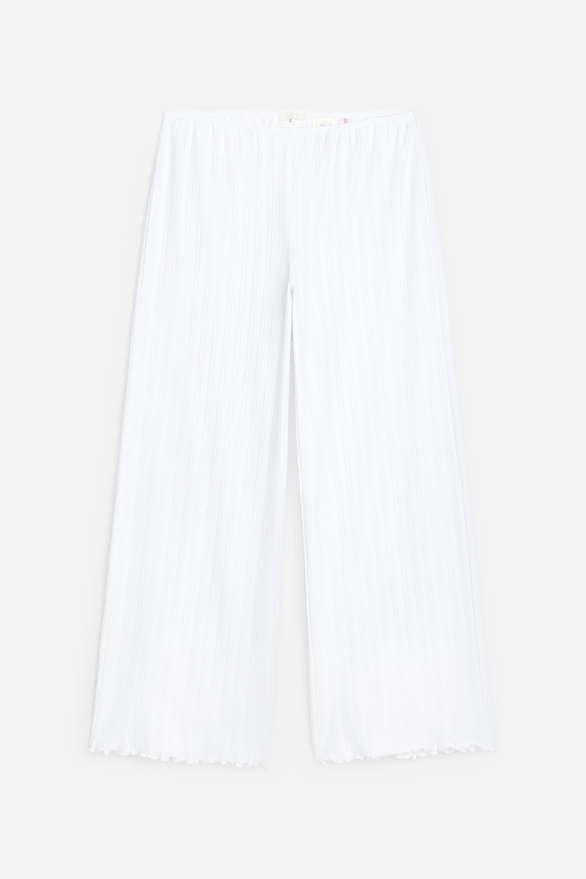 Ver imagen más grande: Pantalones blancos de pierna ancha con textura acanalada se muestran desde el frente, con una cintura lisa que presenta pequeñas etiquetas visibles y dobladillos festoneados.