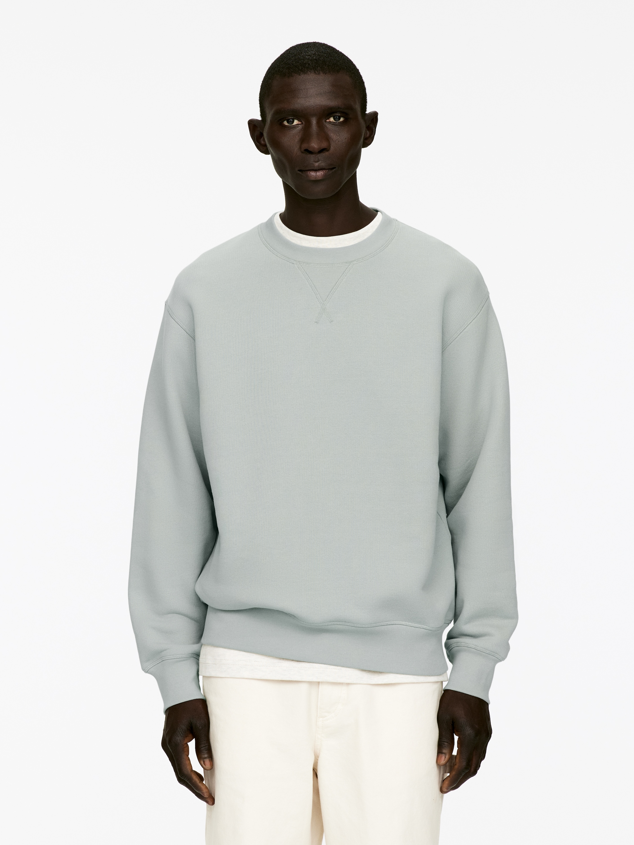 Agrandir l'image: Un sweat-shirt à col rond bleu-vert pâle est présenté de face, avec des poignets côtelés, un ourlet côtelé et un col côtelé avec un détail en V. Il est superposé à un t-shirt blanc, visible au niveau du col et de l'ourlet.