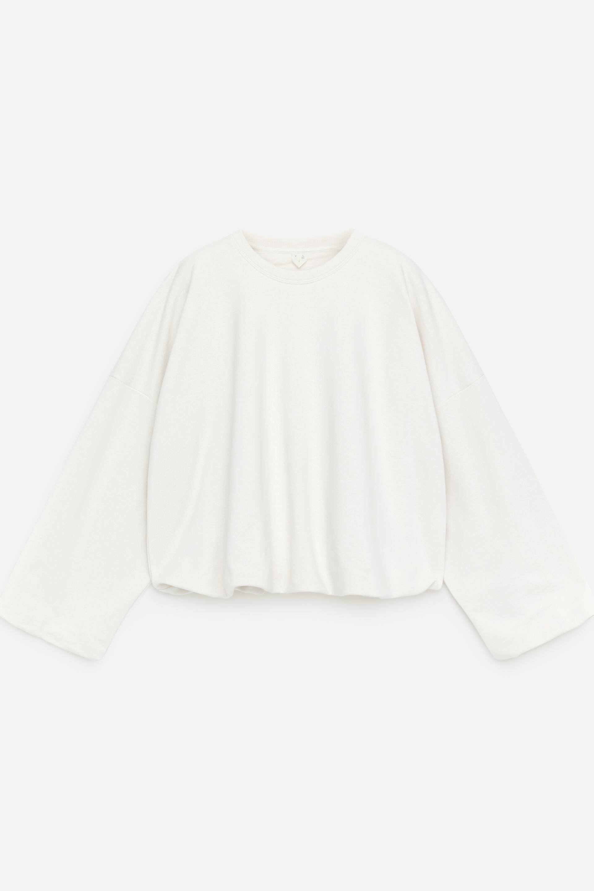 Visa större bild: En vit sweatshirt med rund hals visas framifrån, med en bubbelkant och ballongärmar med rynkade muddar.