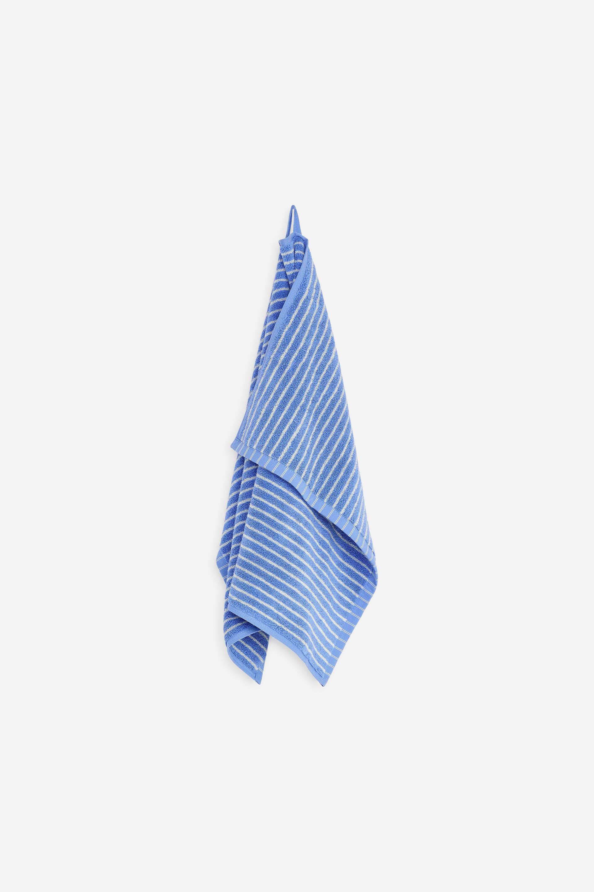 Agrandir l'image: Une serviette à main est suspendue, arborant un motif rayé bleu et blanc sur son tissu éponge, avec une boucle de suspension visible en haut.
