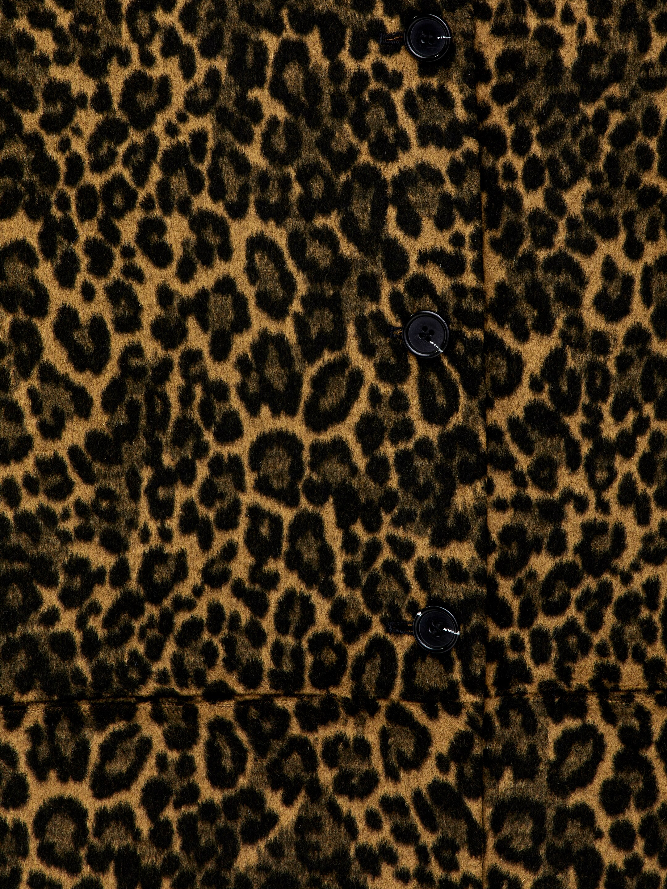 Vis større bilde: En kåpe har et fremtredende leopardmønster med svarte flekker på et teksturert brun-tan stoff. Forsiden av kåpen har en vertikal knappestolpe med tre svarte knapper, og en horisontal søm er synlig over den nedre delen, noe som indikerer en senket midje.