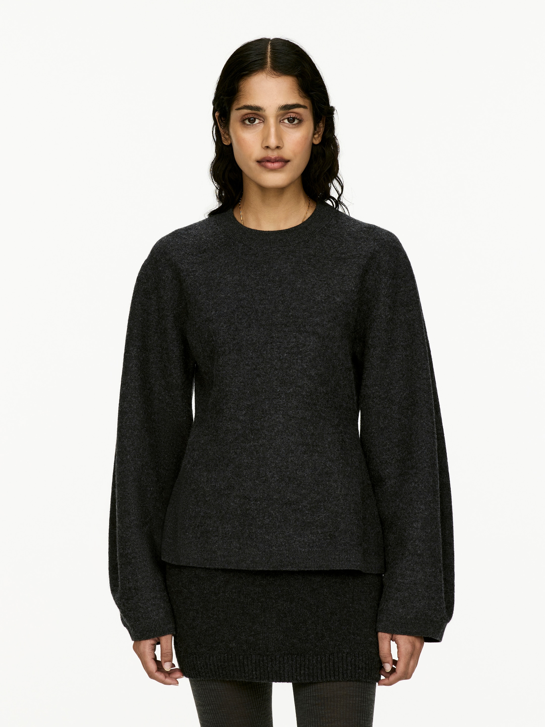 Visualizza immagine più grande: Un maglione grigio scuro con collo rotondo a maglia viene presentato frontale. Le sue lunghe maniche voluminose si restringono verso polsini aderenti e un orlo dritto cade poco sopra una mini gonna coordinata grigio scuro a maglia, che termina con un orlo a costine.