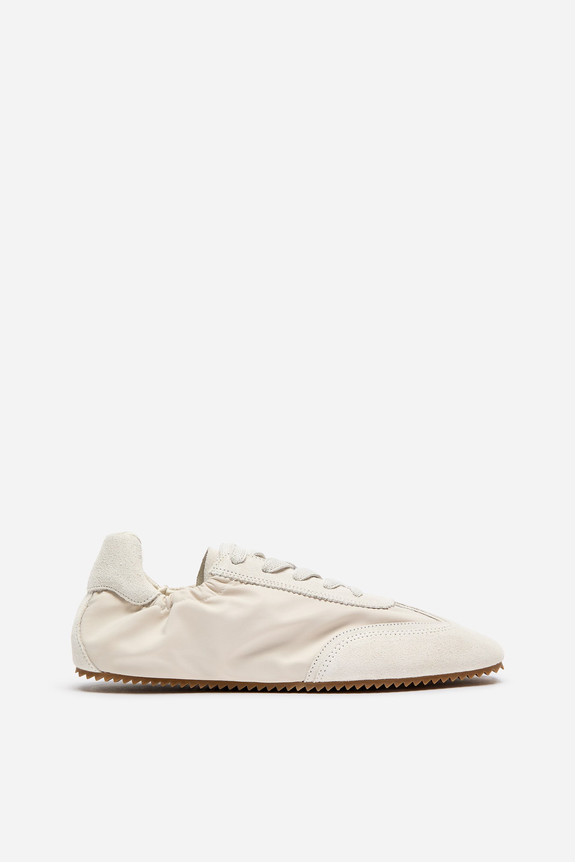 View larger image: A retro-inspired trainer is facing left, featuring a cream-coloured upper crafted from suede and nylon. It showcases lace-up fastening, an elasticated ankle opening, and topstitch detailing on the suede sections, resting on a brown ridged sole.