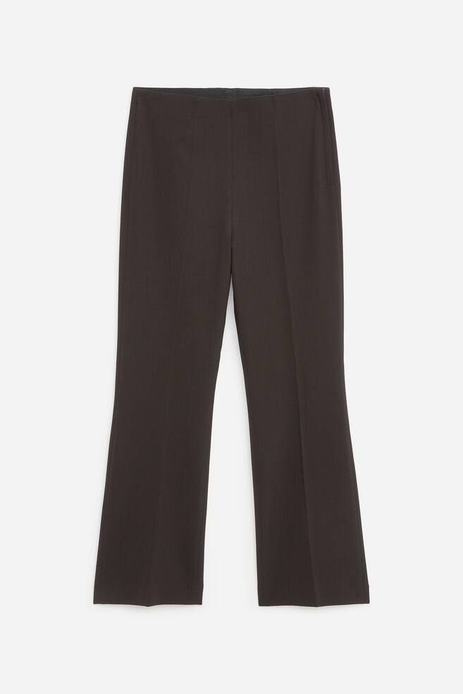 These dark brown tailored trousers are shown from the front, featuring a clean, seamless waistband and sharp pressed creases running down the centre of each leg. The trousers display a slim-fit, straight-leg silhouette with a discreet side zip closure on the upper right. - 1