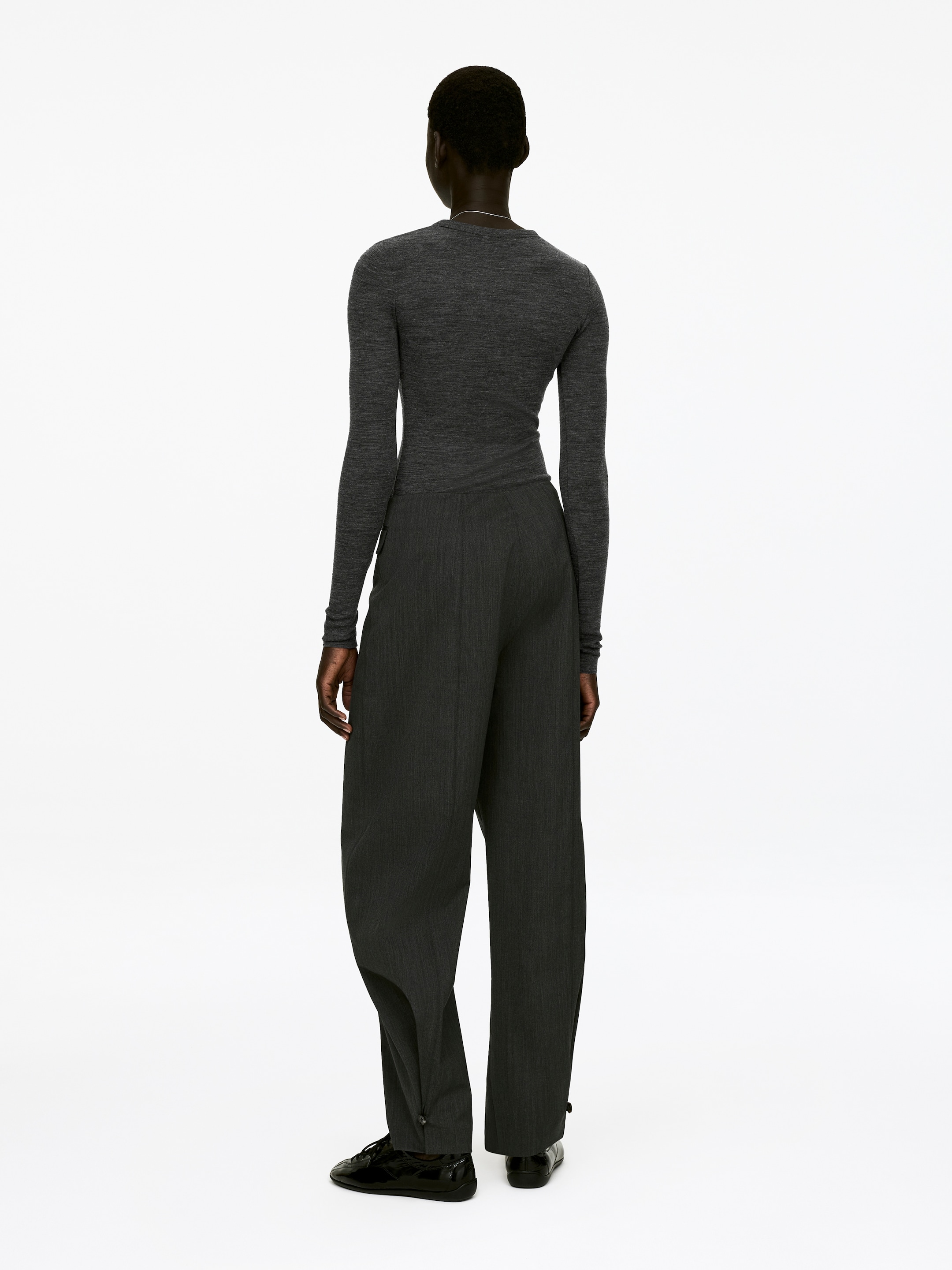 Grösseres Bild ansehen: Das Model trägt ein dunkelgraues, langärmliges, eng anliegendes Oberteil mit rundem Ausschnitt, das in eine dunkelgraue Hose gesteckt ist.