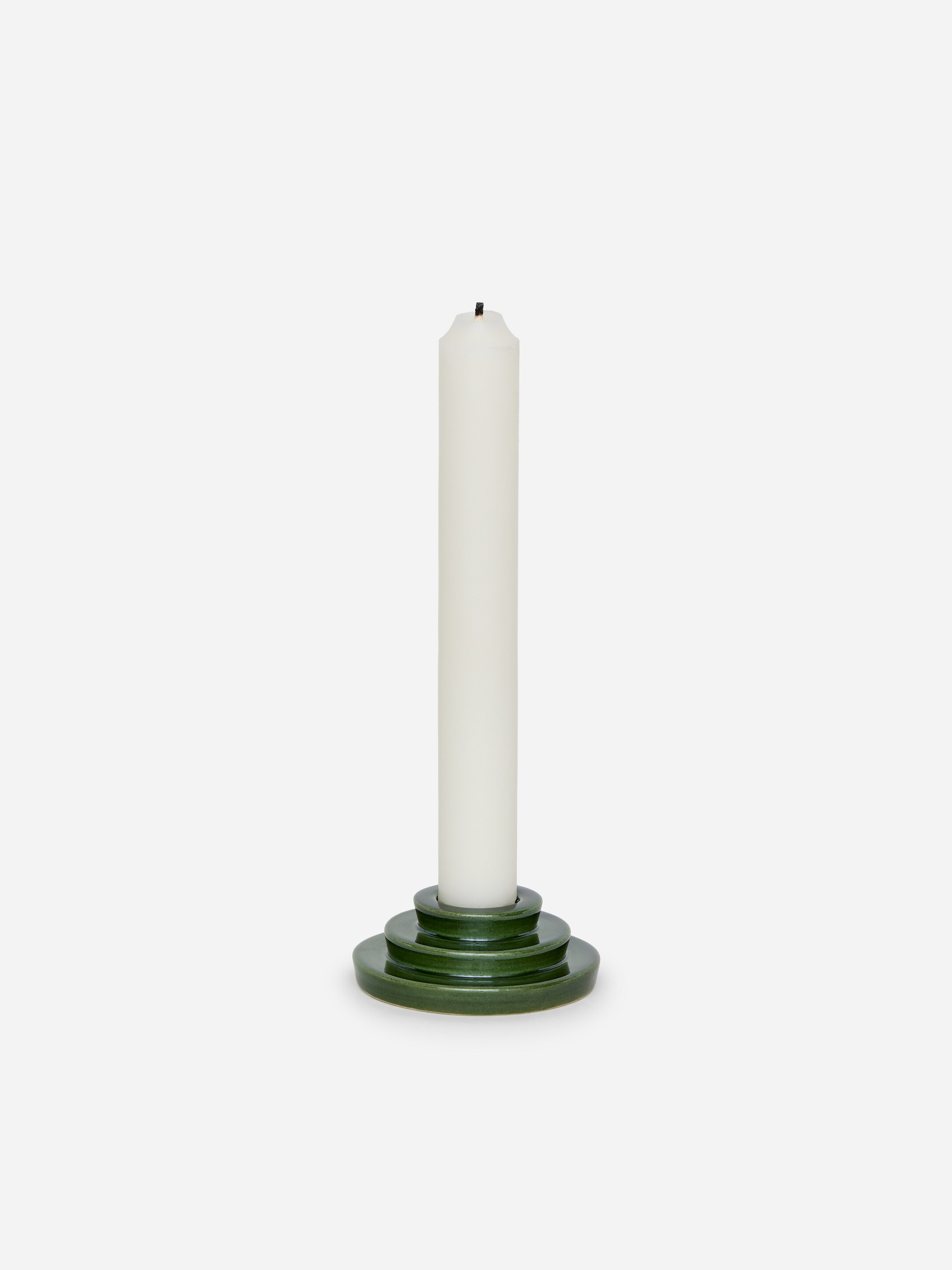 Ver imagen más grande: Una vela cilíndrica blanca, con una mecha negra visible, está de pie en un candelero verde oscuro de niveles. El candelero brillante presenta tres capas circulares apiladas.