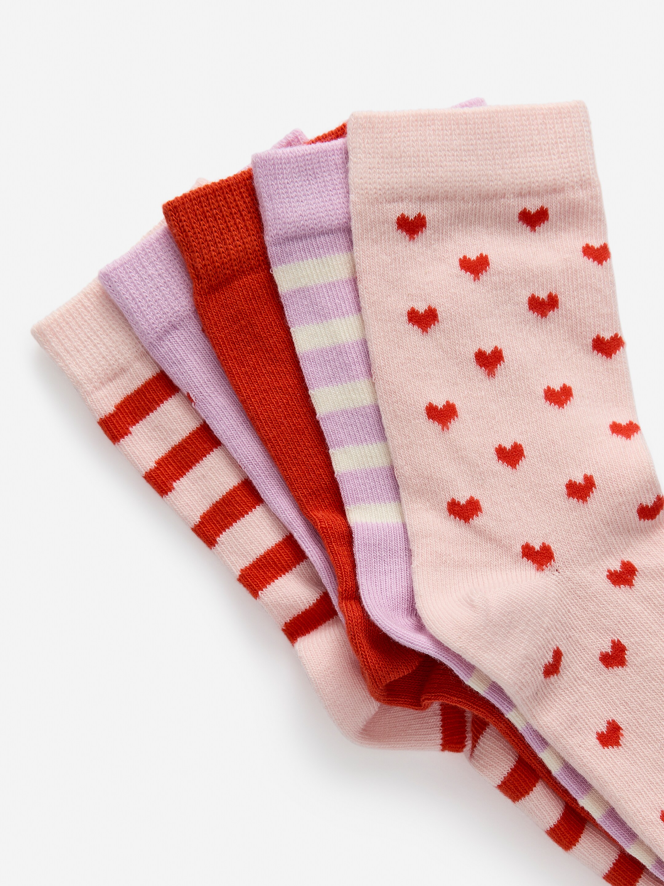 Grösseres Bild ansehen: Fünf Socken sind aufgefächert und zeigen ihre Vorderseiten, jede mit einem gerippten Bündchen. Sie zeigen eine Vielzahl von Mustern, darunter hellrosa mit roten horizontalen Streifen, einfarbig rot, hellviolett mit hellcremefarbenen horizontalen Streifen und hellrosa mit verstreuten roten Herzmustern. Die fünfte Socke zeigt ein schlichtes hellrosa Bündchen.