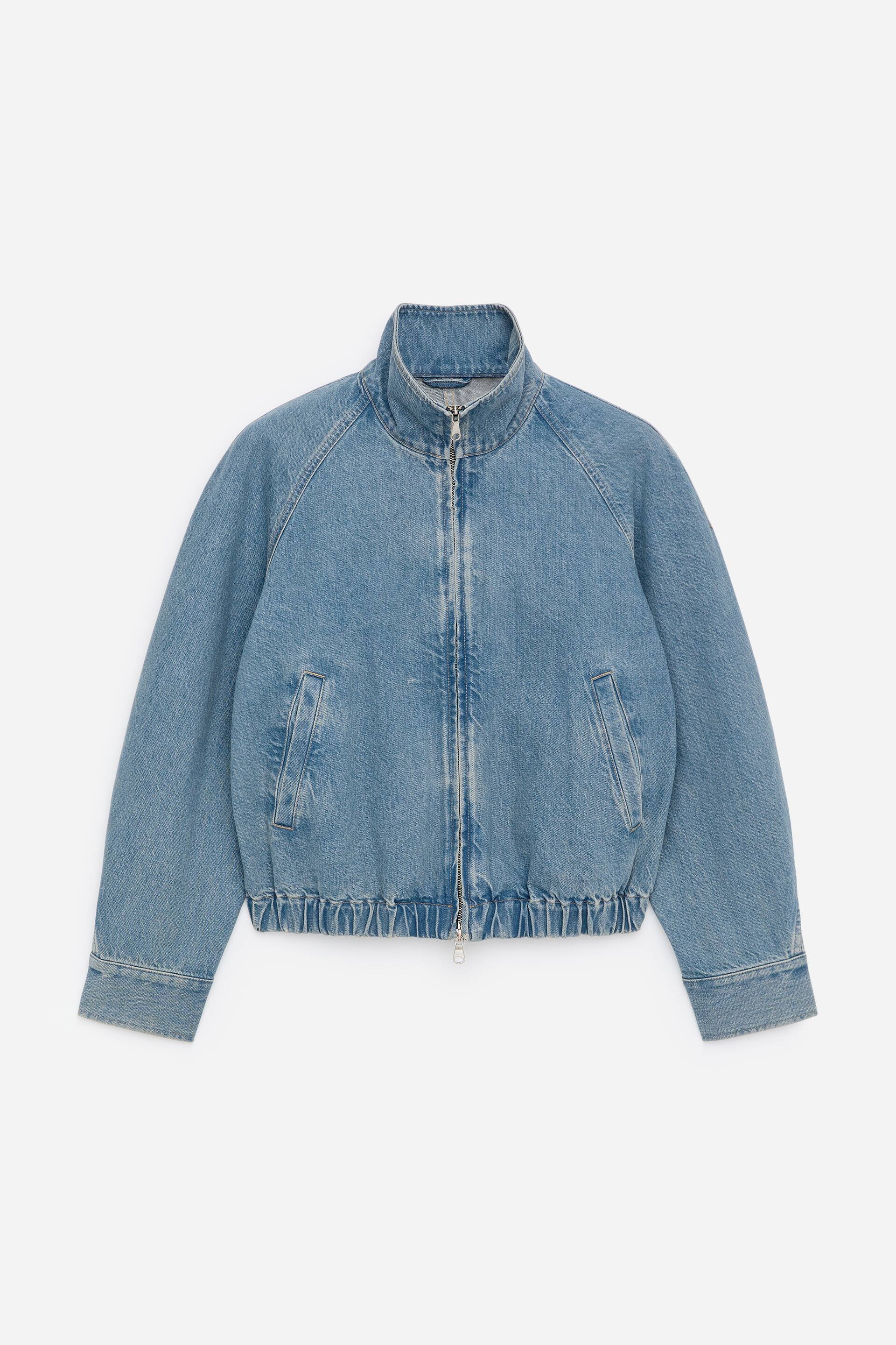 Agrandir l'image: Une veste en jean courte en coton bleu clair présente son DEVANT, défini par une taille élastiquée et des manches torsadées. Elle est dotée d'un col cheminée, d'une fermeture zippée centrale et de deux poches avant en biais.