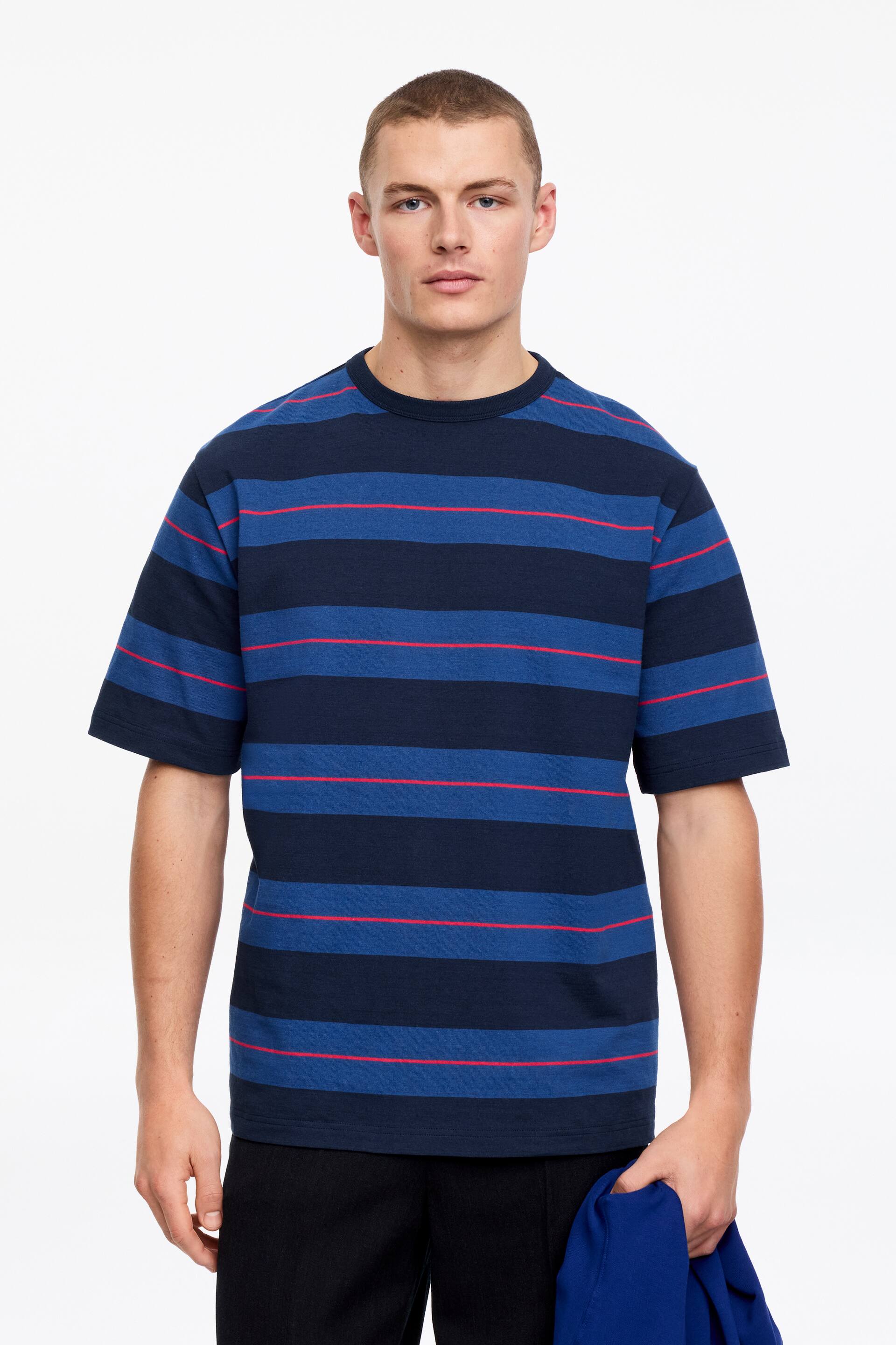 Grotere afbeelding bekijken: Een T-shirt met horizontale strepen, afwisselend tussen marineblauw en koningsblauw, met dunne rode lijnen. Het is ontworpen met een ronde hals en korte mouwen.