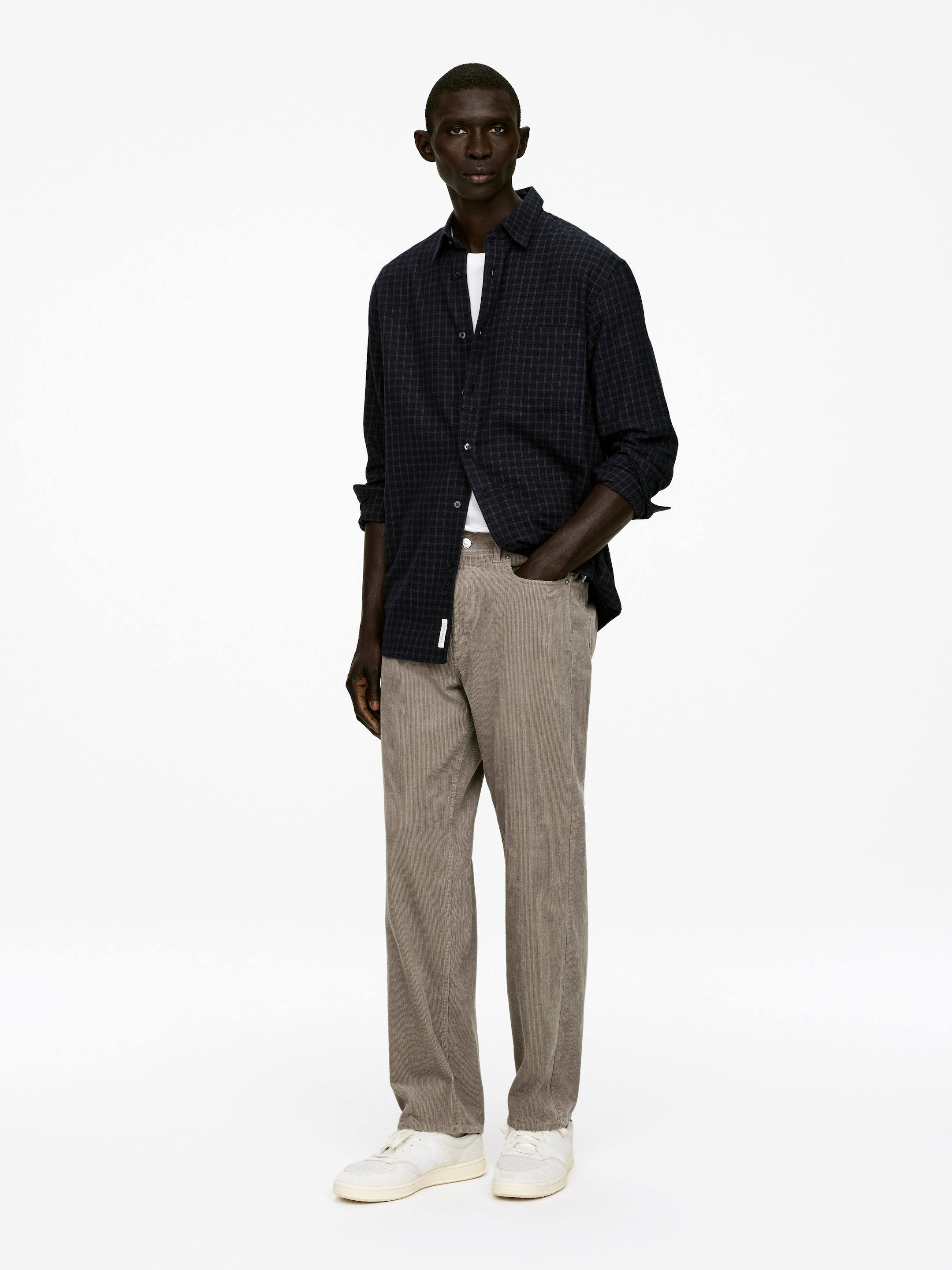 Visualizza immagine più grande: Pantaloni in velluto a coste di cotone marrone chiaro con un classico stile a 5 tasche, vita media e una silhouette ampia e dritta sono indossati dalla modella, la cui mano sinistra è appoggiata in una tasca anteriore.